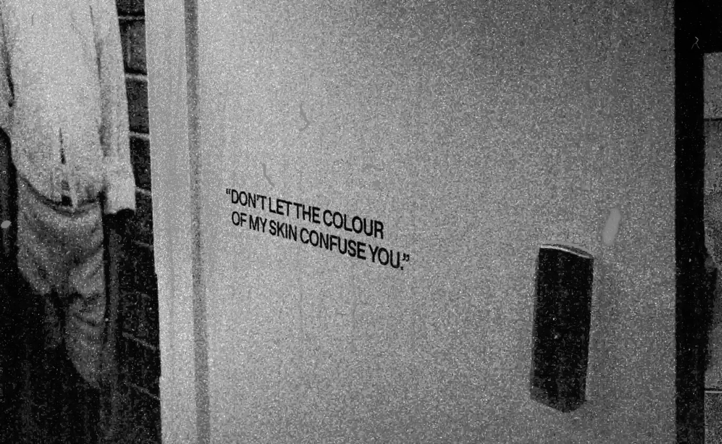 A close-up of a textured surface with a partial quote that reads 'DON'T LET THE COLOUR OF MY SKIN CONFUSE YOU' in black text.