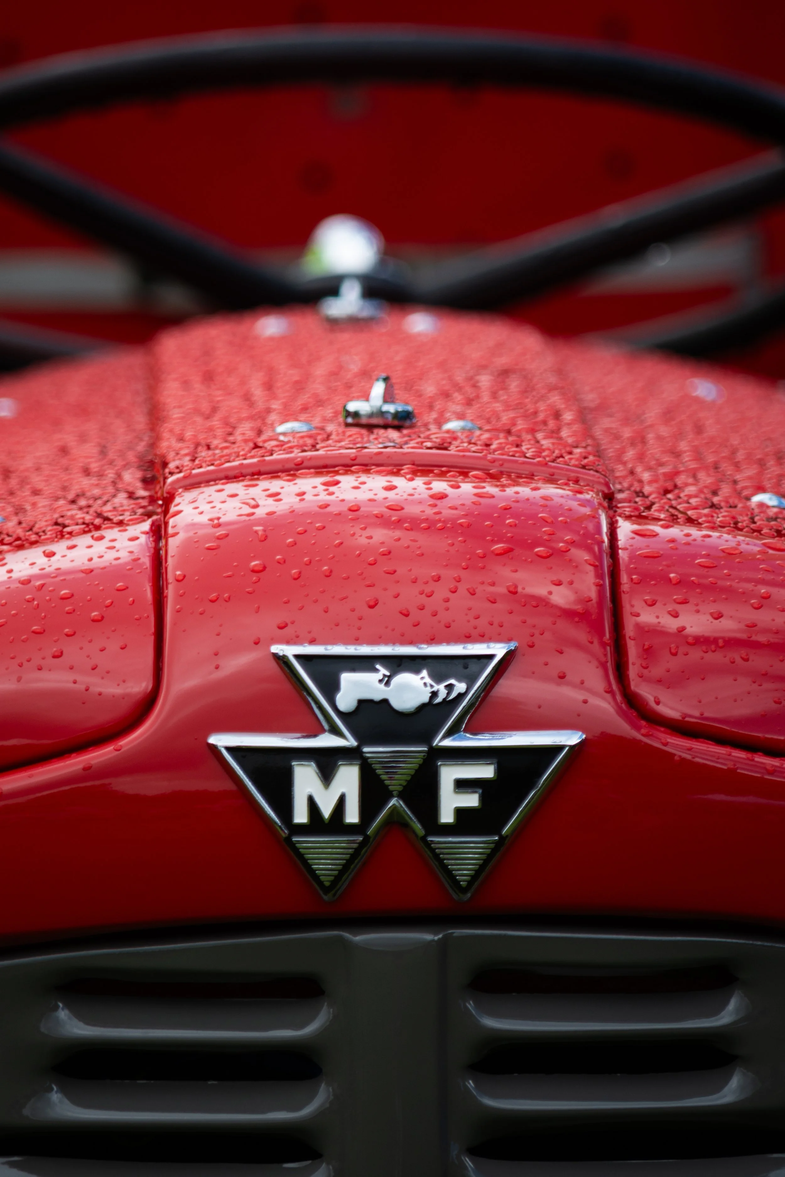 Close-up of a red vintage Mercedes-Benz car hood with water droplets, showing the Mercedes-Benz logo and front grille.