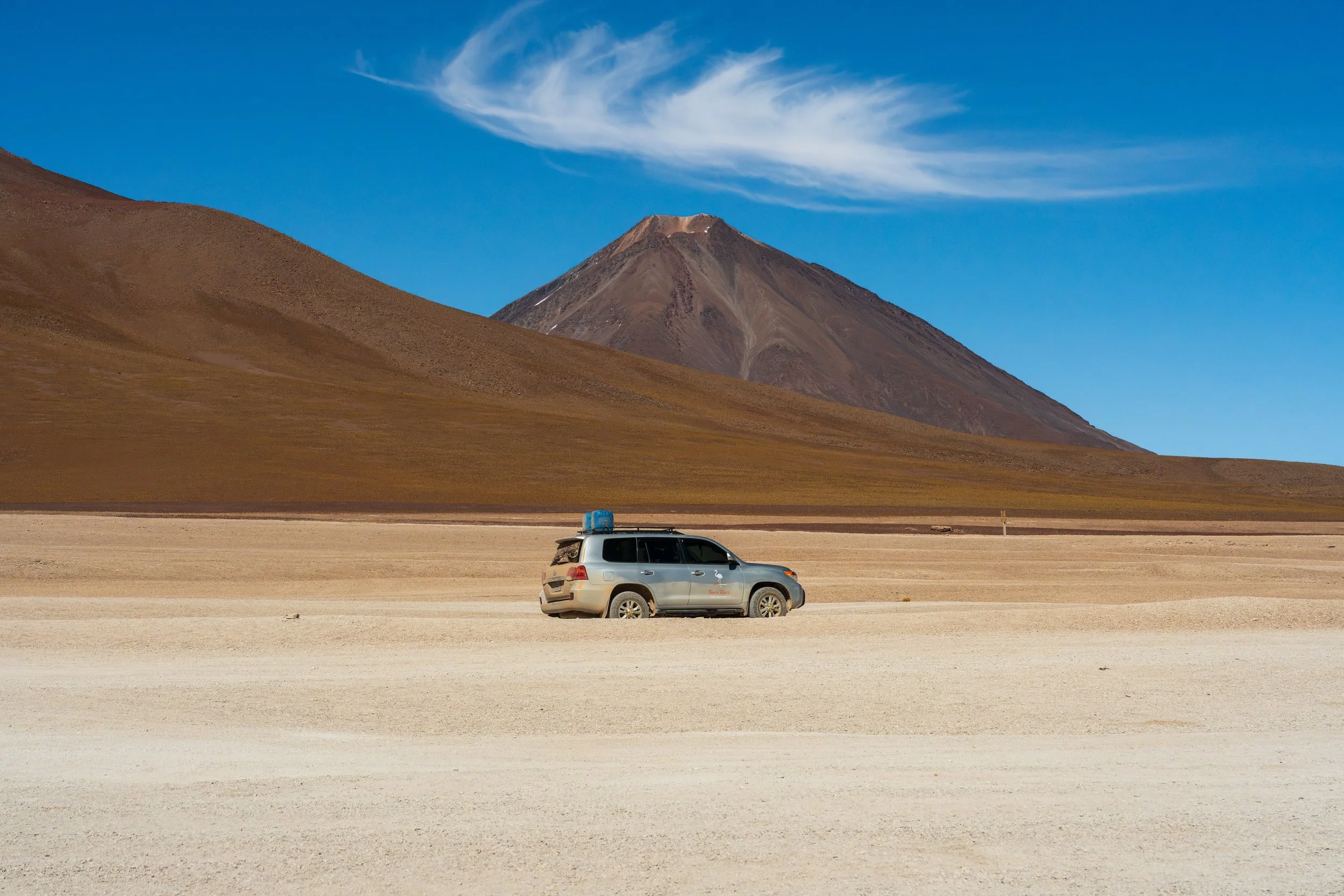 Véhicule 4x4 traversant l'altiplano du Sud Lipez devant un volcan bolivien