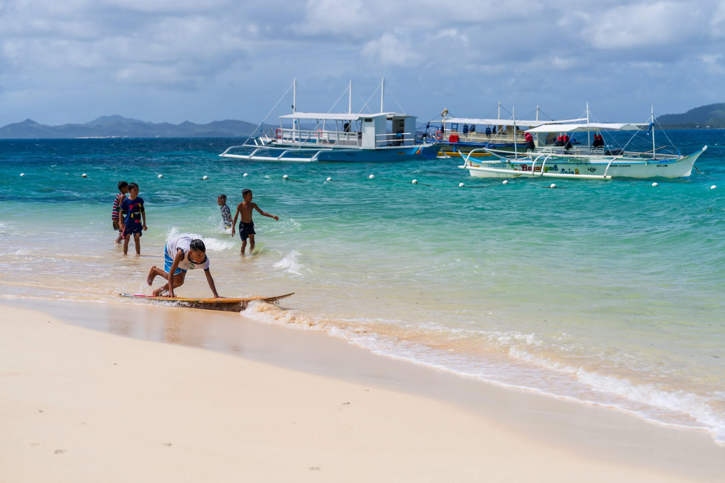 Enfants jouant sur la plage devant les bancas de l'island hopping à Siargao