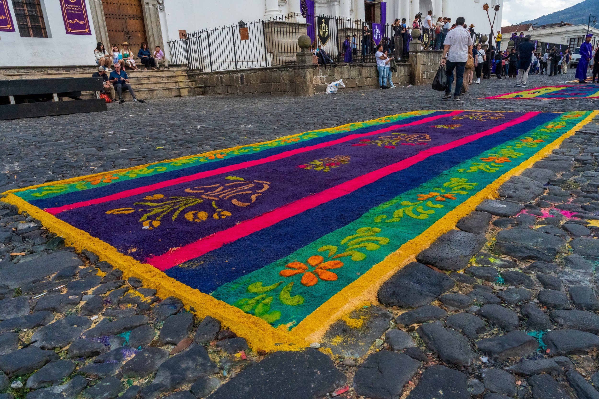 Tapis de sciure à bandes violettes, roses et vertes, motifs floraux, sur les pavés
