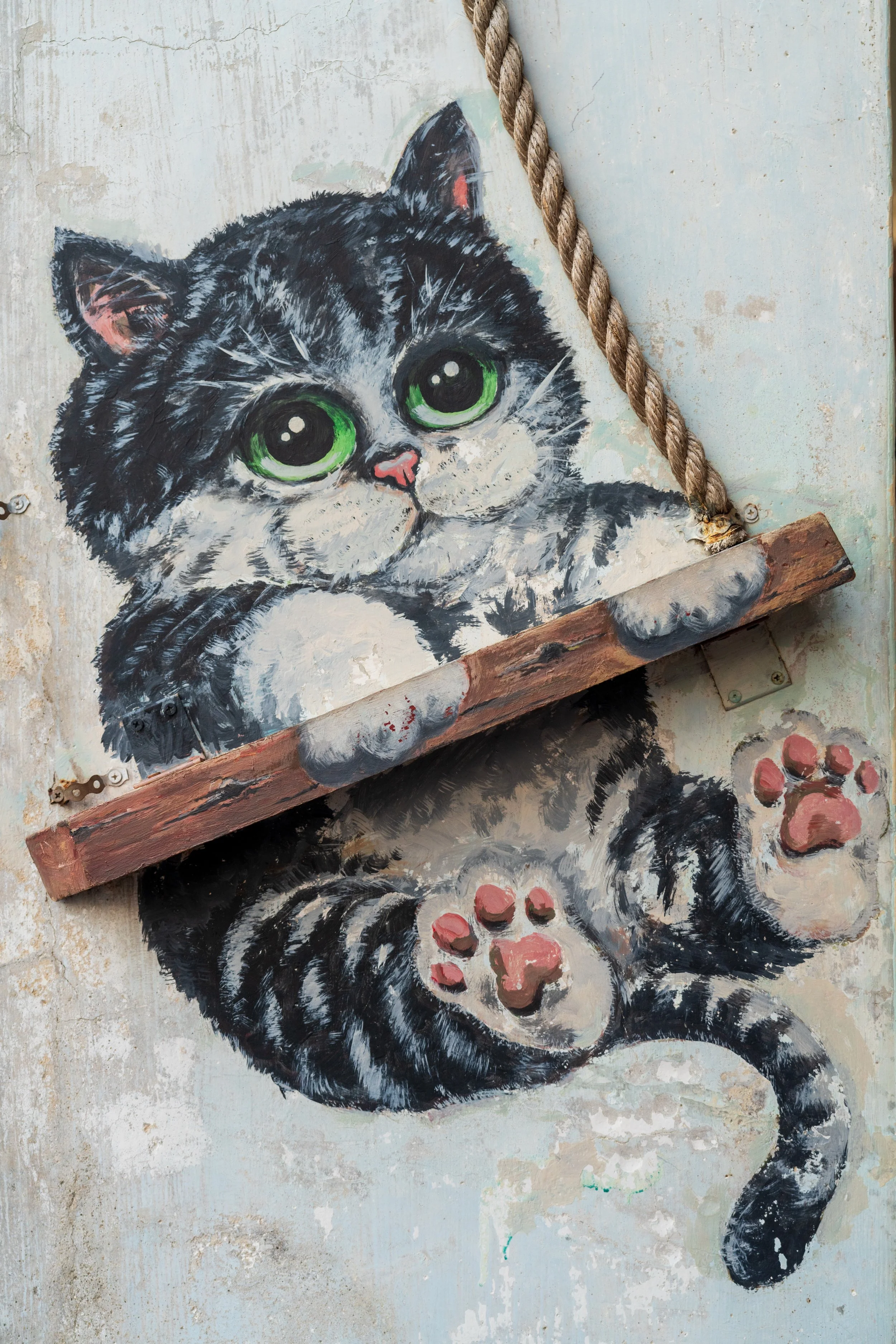 Grande fresque d'un chaton gris et blanc jouant sur une balançoire en bois, street art de Georgetown à Penang
