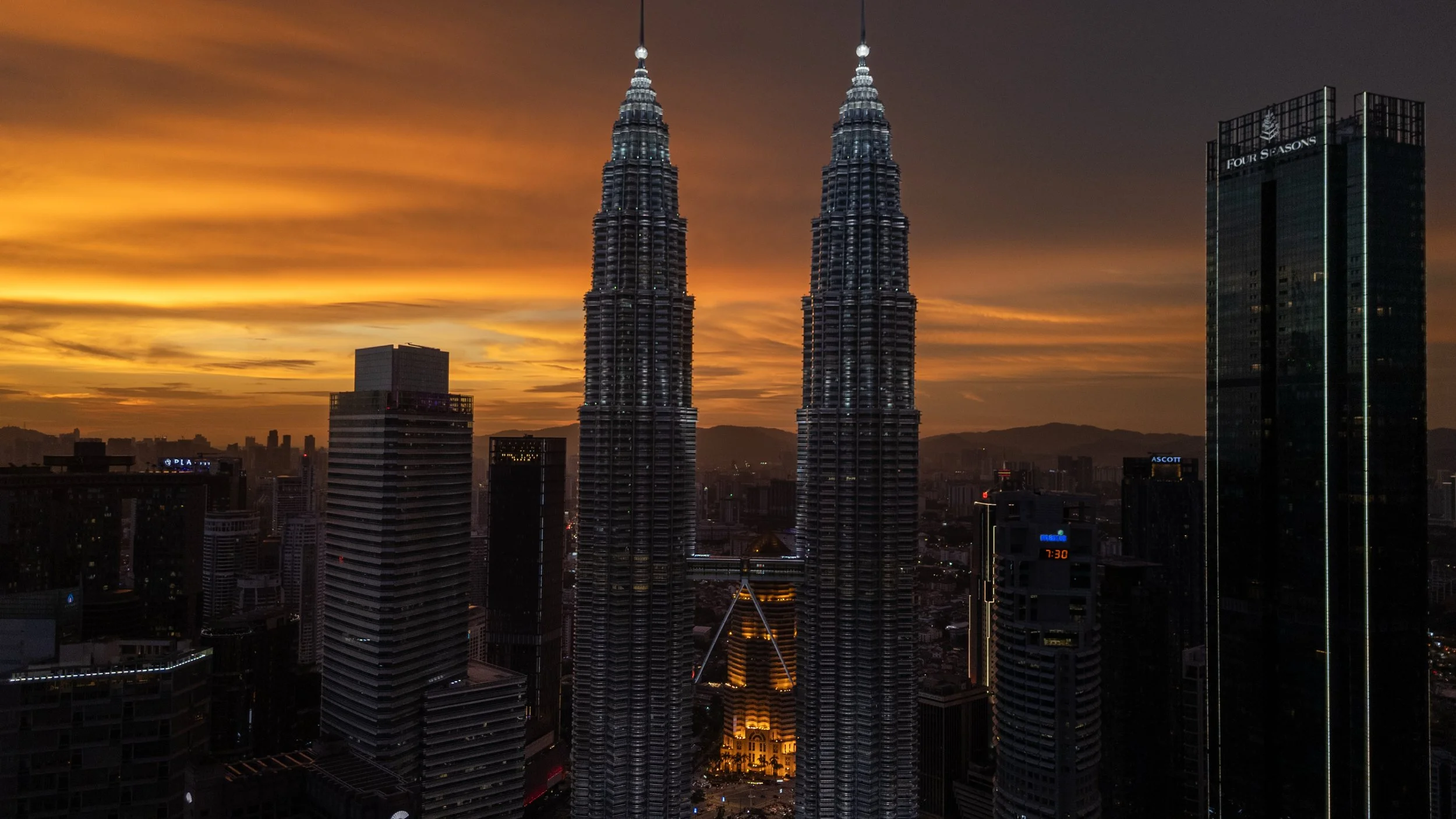 Tours Petronas au coucher du soleil, silhouettes dorées sur le ciel orangé de Kuala Lumpur