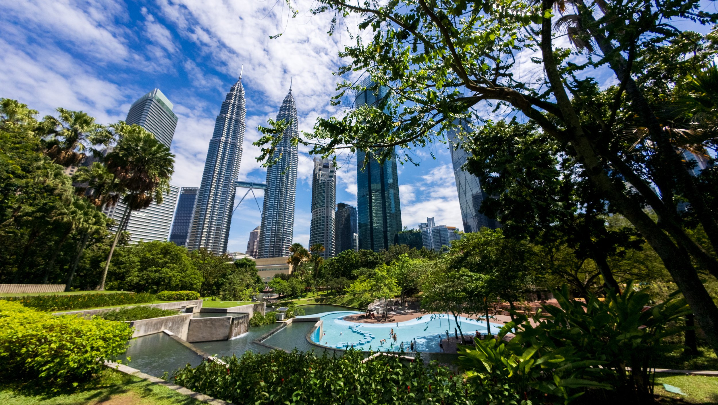 Tours Petronas vues depuis un jardin, entre feuillage et piscine à débordement