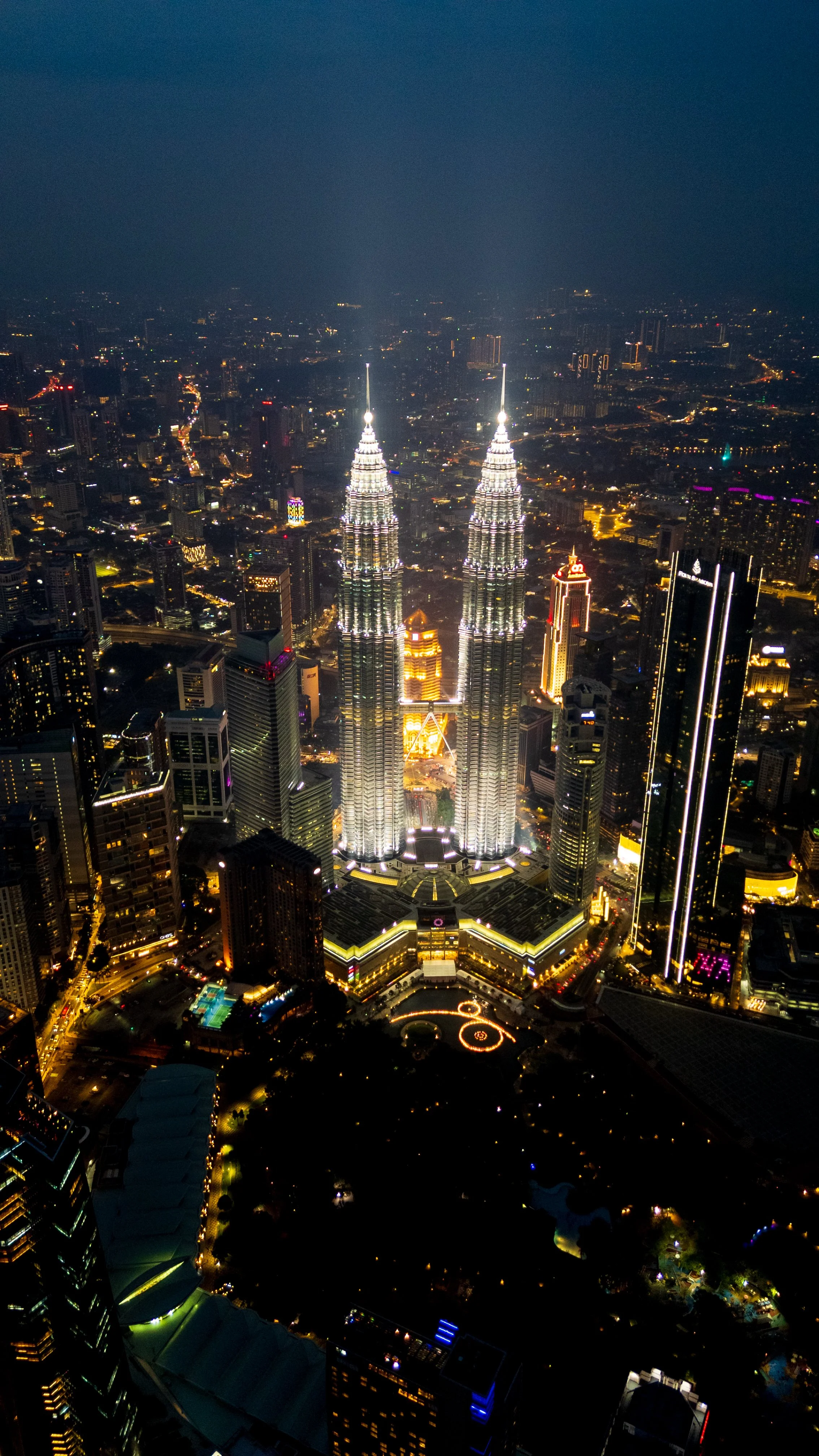 Tours Petronas illuminées de nuit, vue plongeante depuis un rooftop sur les toits de Kuala Lumpur