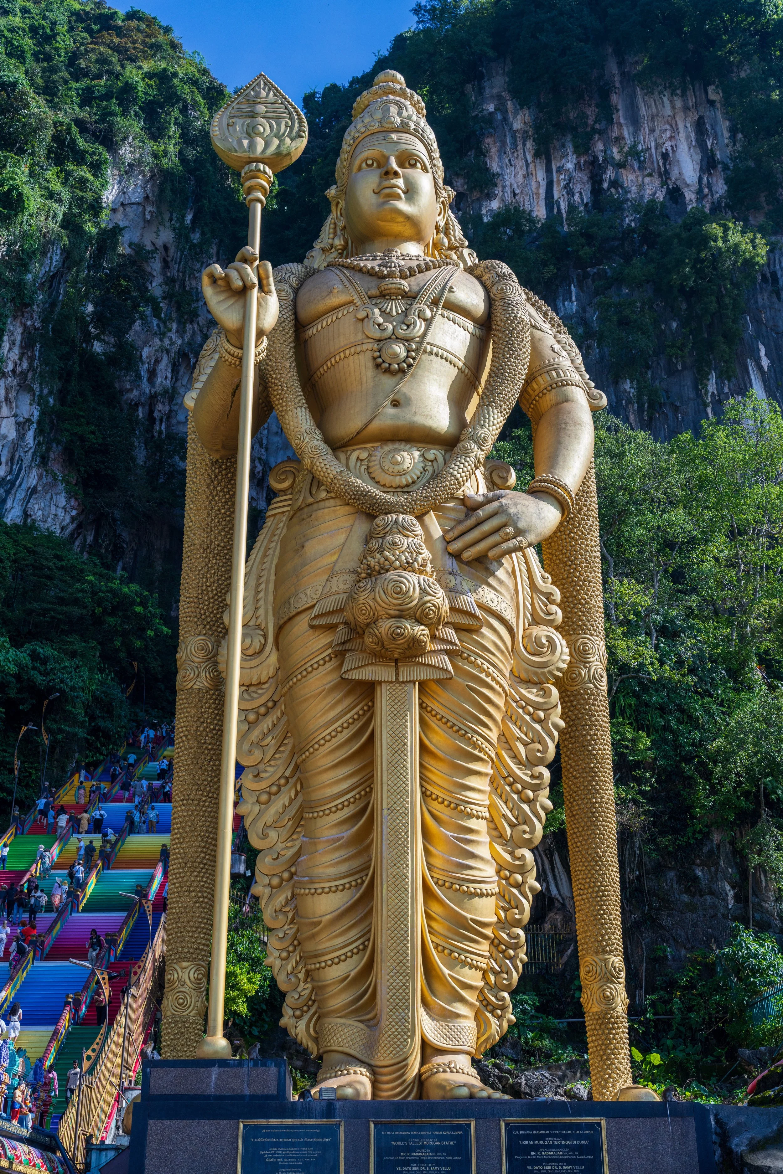 Statue dorée de Murugan au pied de la falaise calcaire de Batu Caves, escalier coloré menant à la grotte