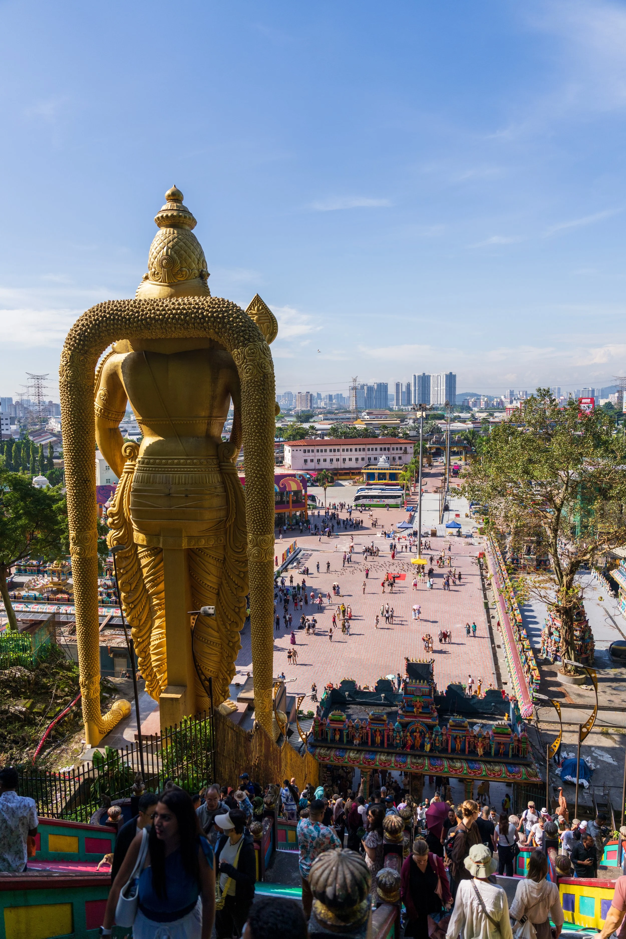 Vue aérienne de la statue dorée de Murugan et de l'esplanade de Batu Caves, avec la skyline de Kuala Lumpur en arrière-plan