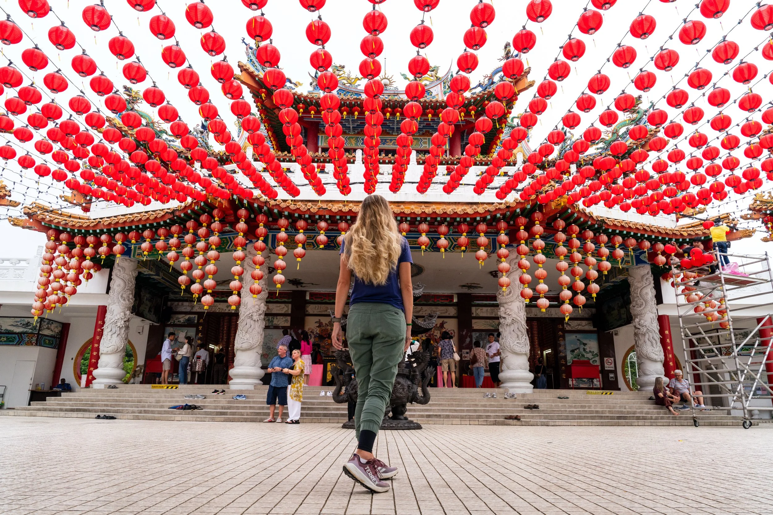 Femme de dos sous une allée de lanternes rouges suspendues devant un temple chinois de Kuala Lumpur