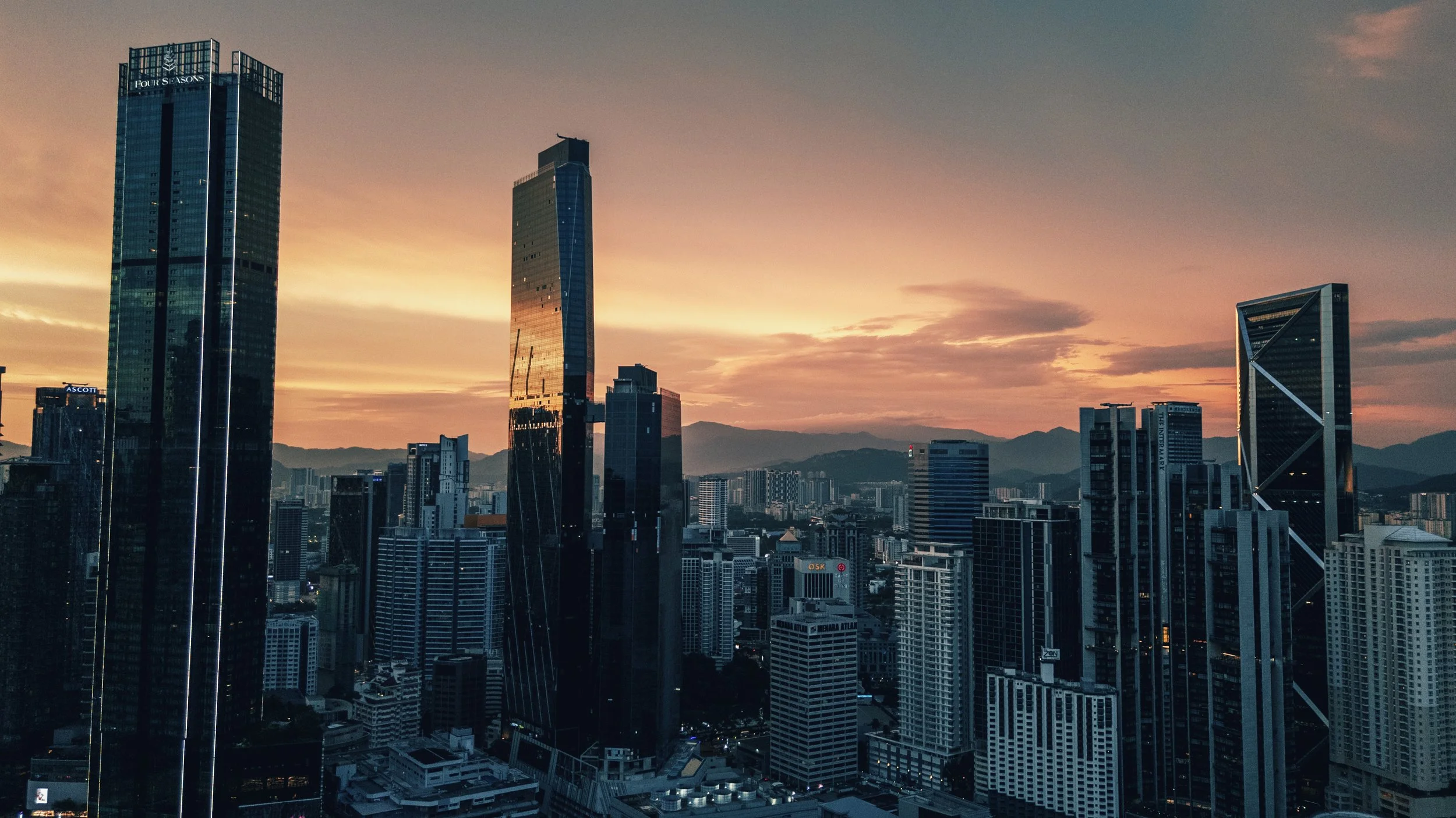 Vue aérienne au drone du skyline de Kuala Lumpur au coucher du soleil, gratte-ciels du centre-ville silhouettés sur un ciel orangé