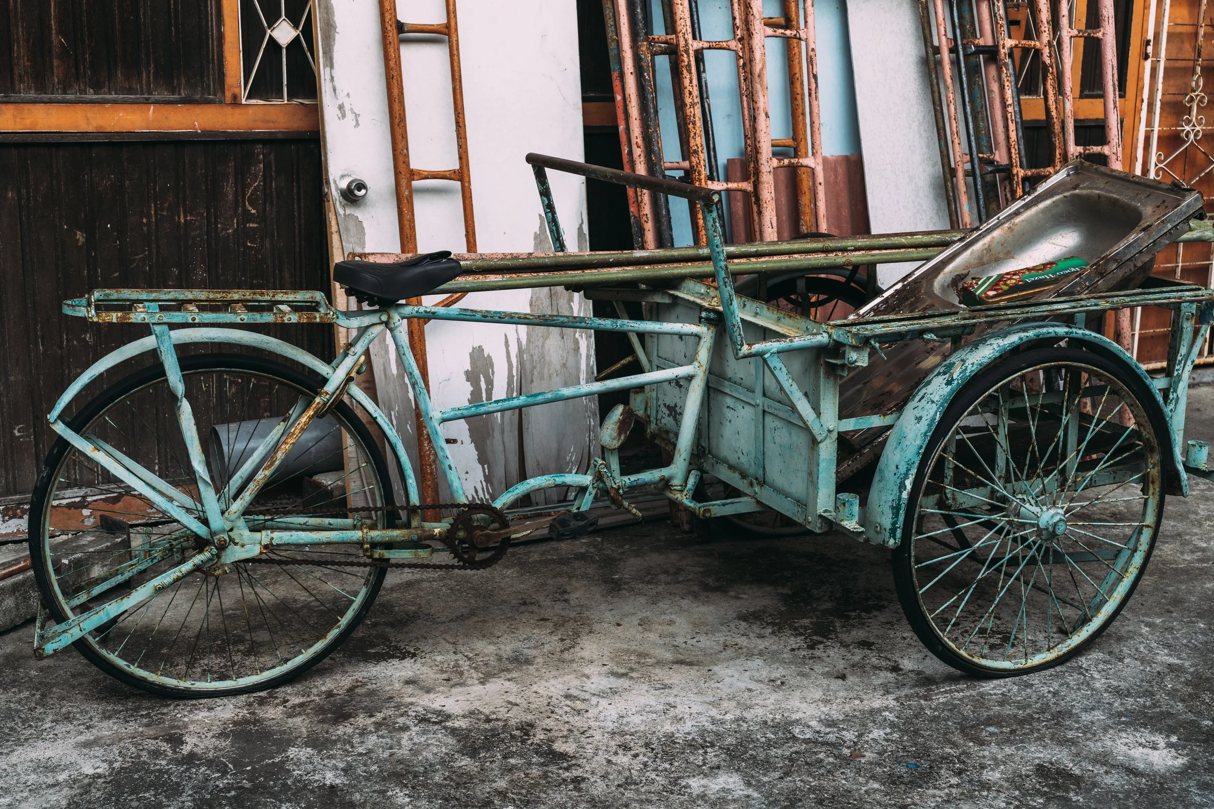 Vieux trishaw en métal rouillé garé contre une façade délavée dans le quartier du street art de Georgetown, Penang