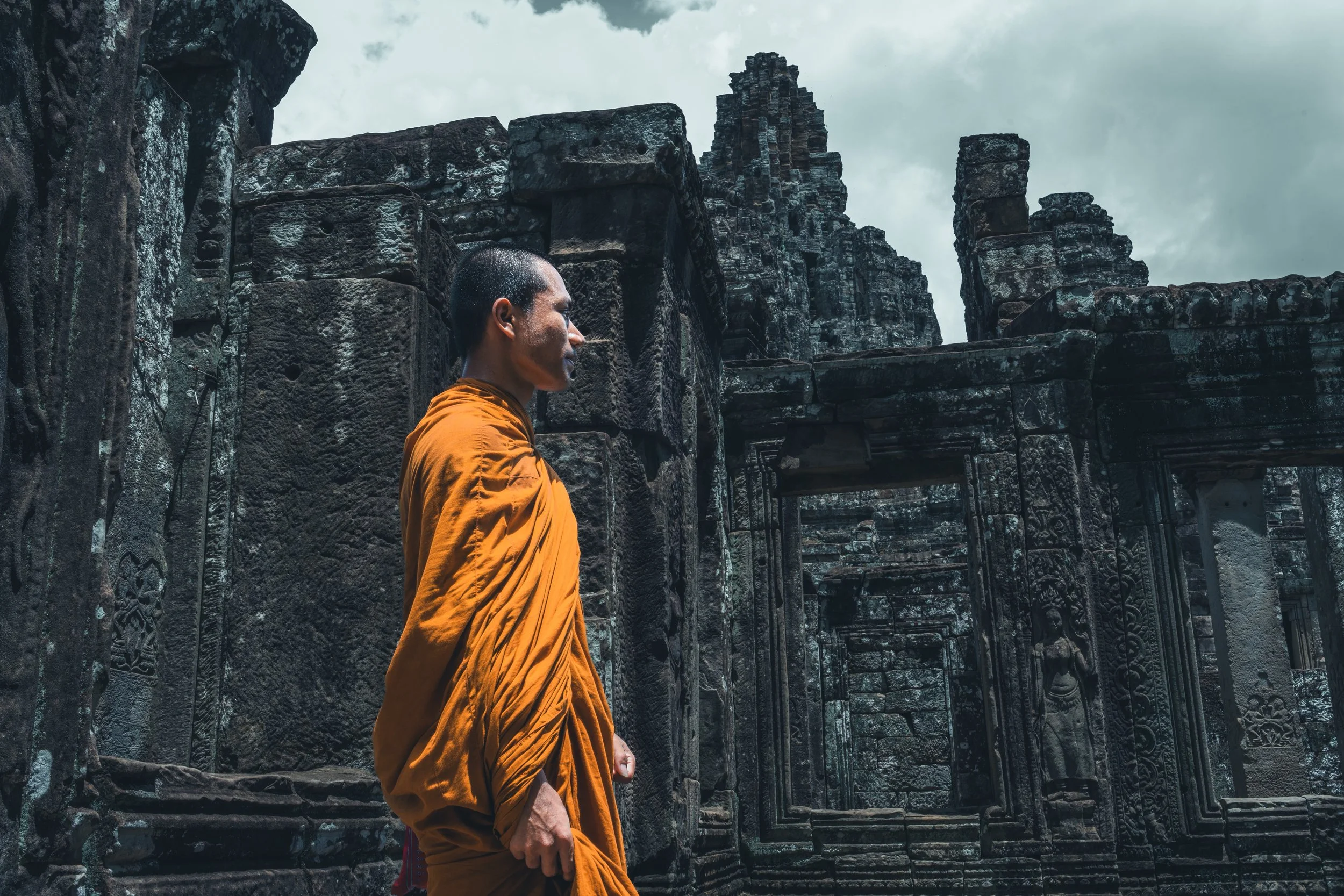 Moine bouddhiste en robe safran devant les visages sculptés du Bayon