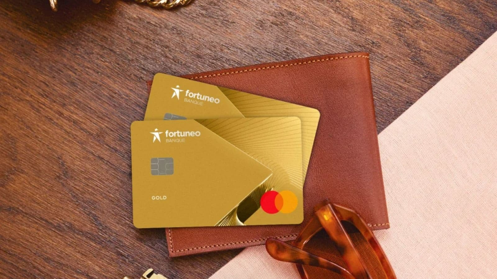 Deux cartes bancaires Fortuneo dorées devant un portefeuille en cuir