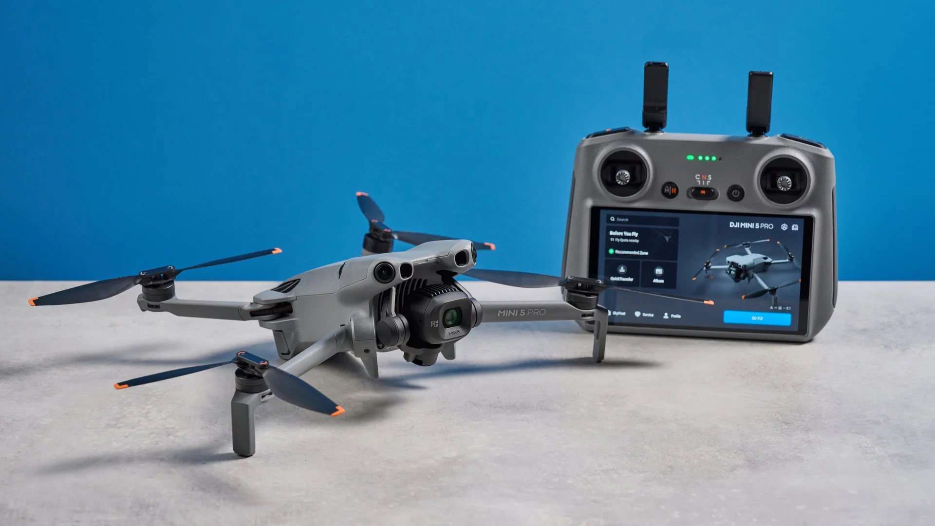 DJI Mini 5 Pro déplié à côté de sa radiocommande RC 2 à écran, sur fond bleu studio