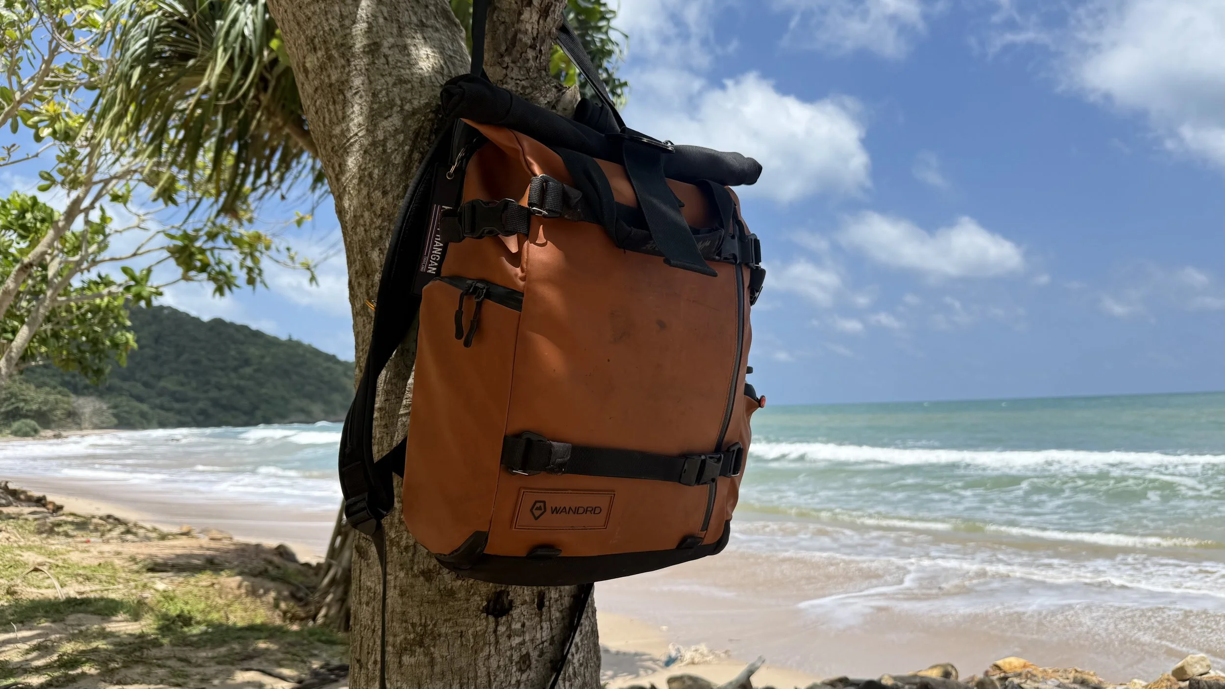 Sac à dos de voyage orange posé contre un arbre sur une plage tropicale