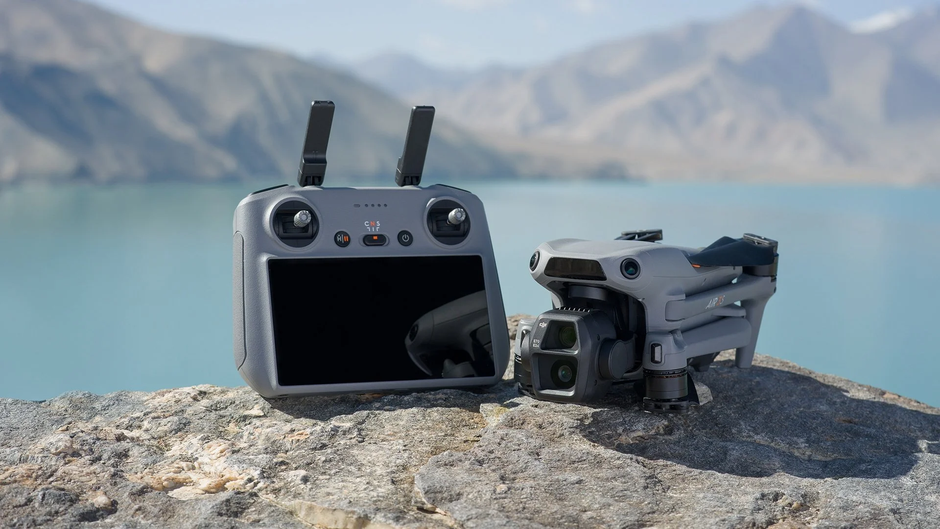 DJI Air 3S plié posé sur un rocher à côté de sa radiocommande RC 2, devant un lac de montagne