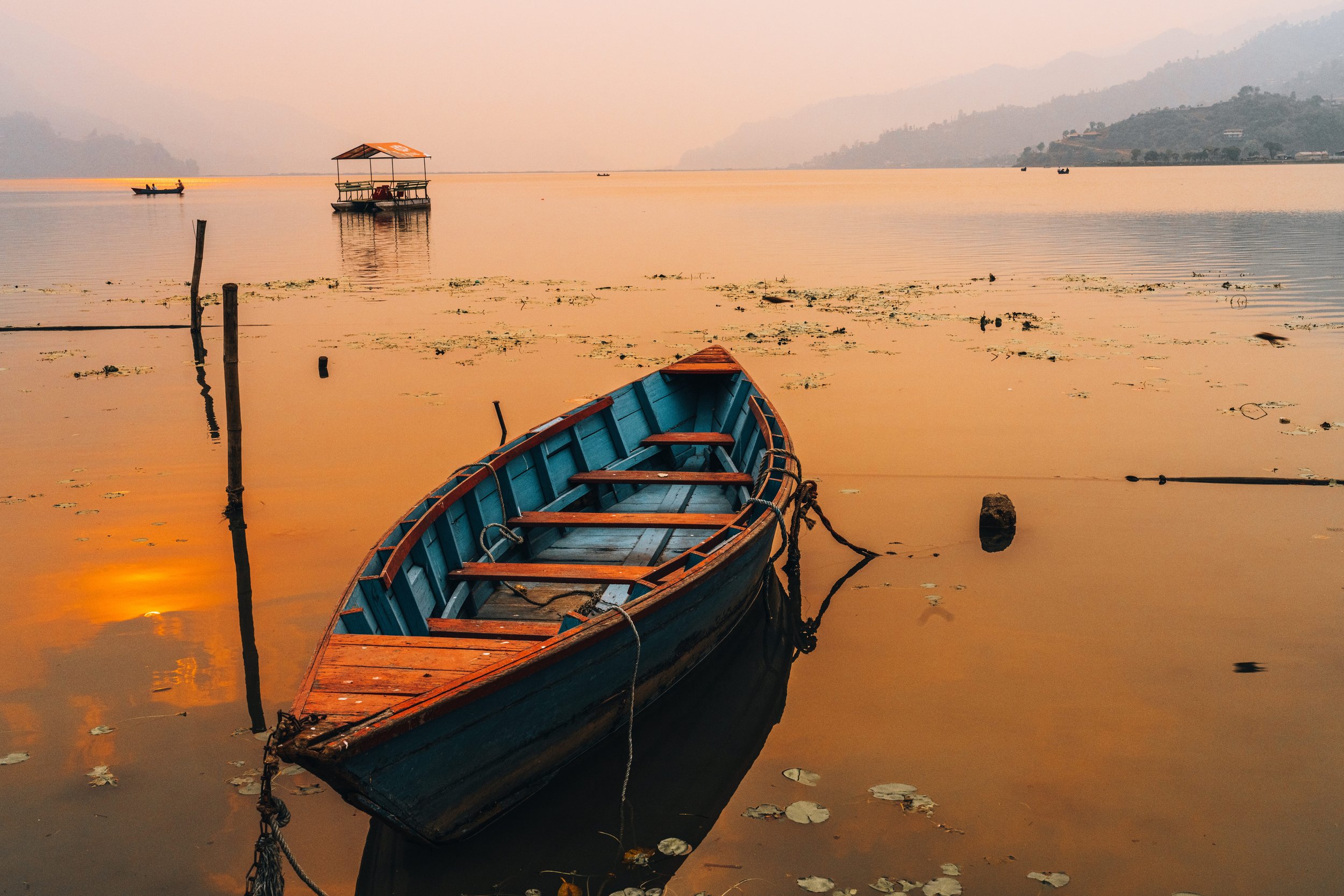 Barque en bois sur les eaux dorées du lac Phewa au lever du jour à Pokhara