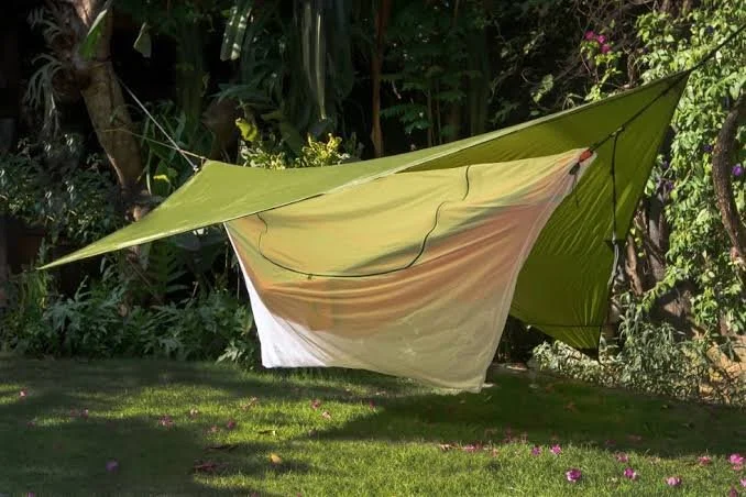 Hamac de voyage abrité sous une bâche et une moustiquaire dans un jardin