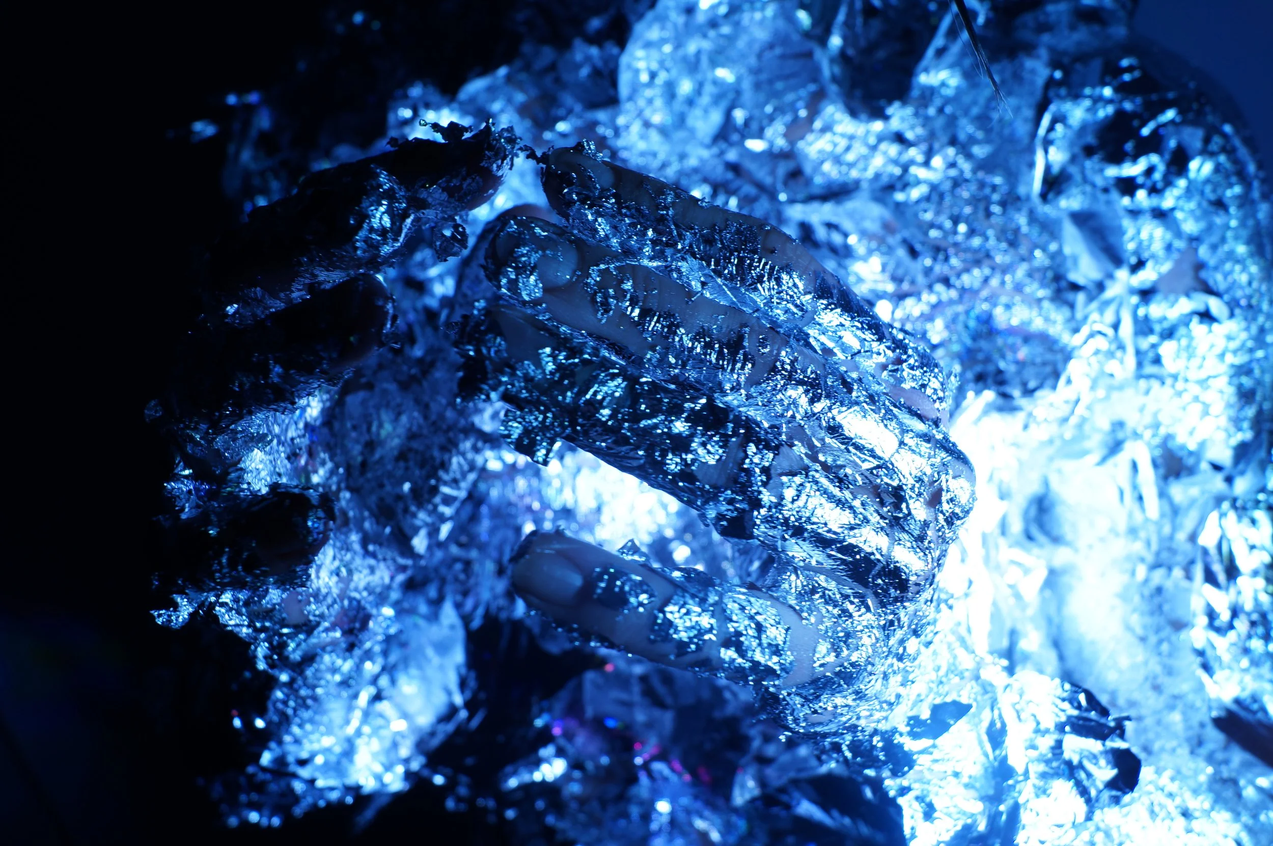 Close-up of a hand covered in reflective material and illuminated with blue light during a performance by Marina Dessau.