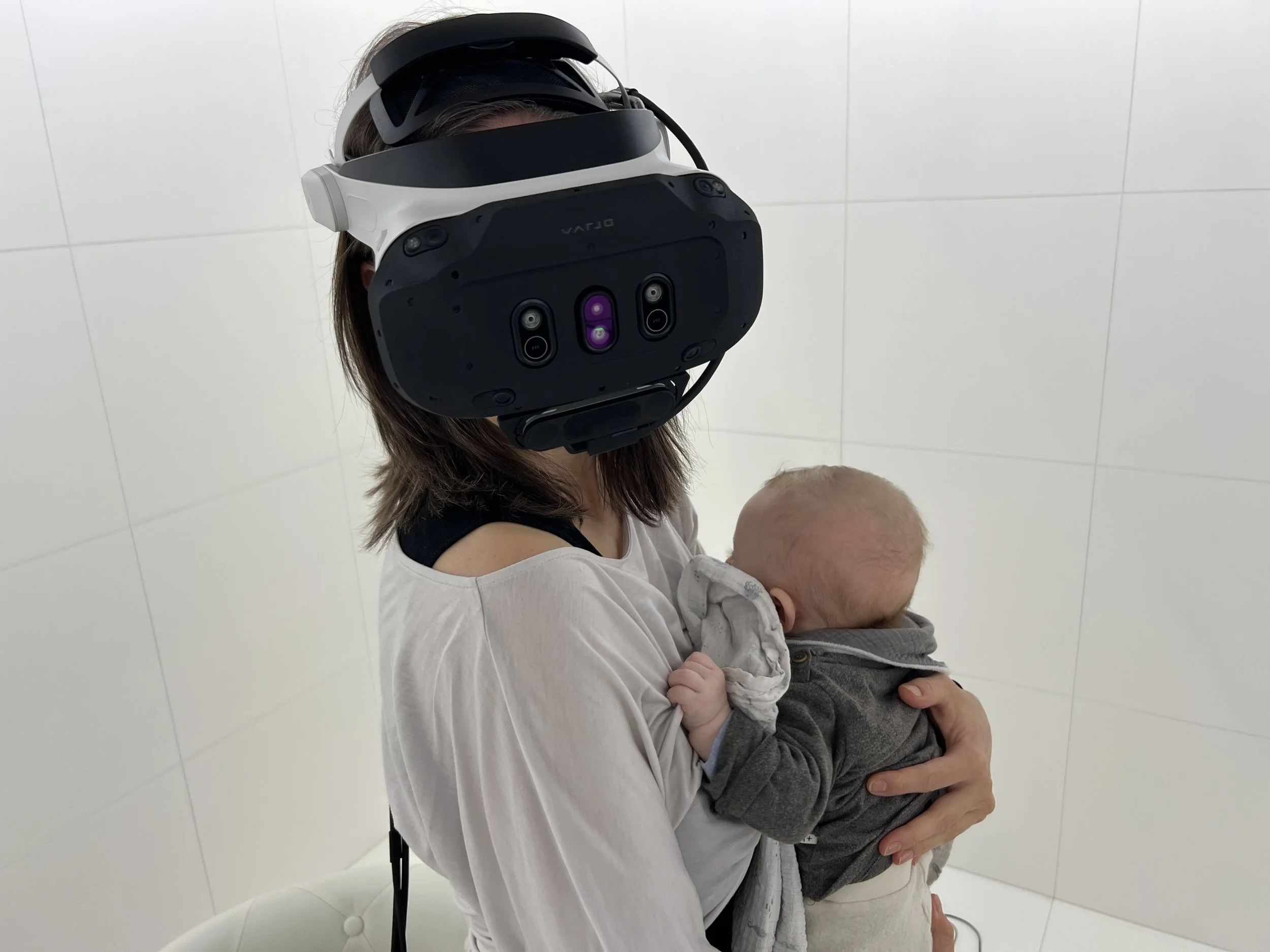 Marina Dessau wearing a VR headset while holding a baby during her artistic research into perception, embodiment and technology.