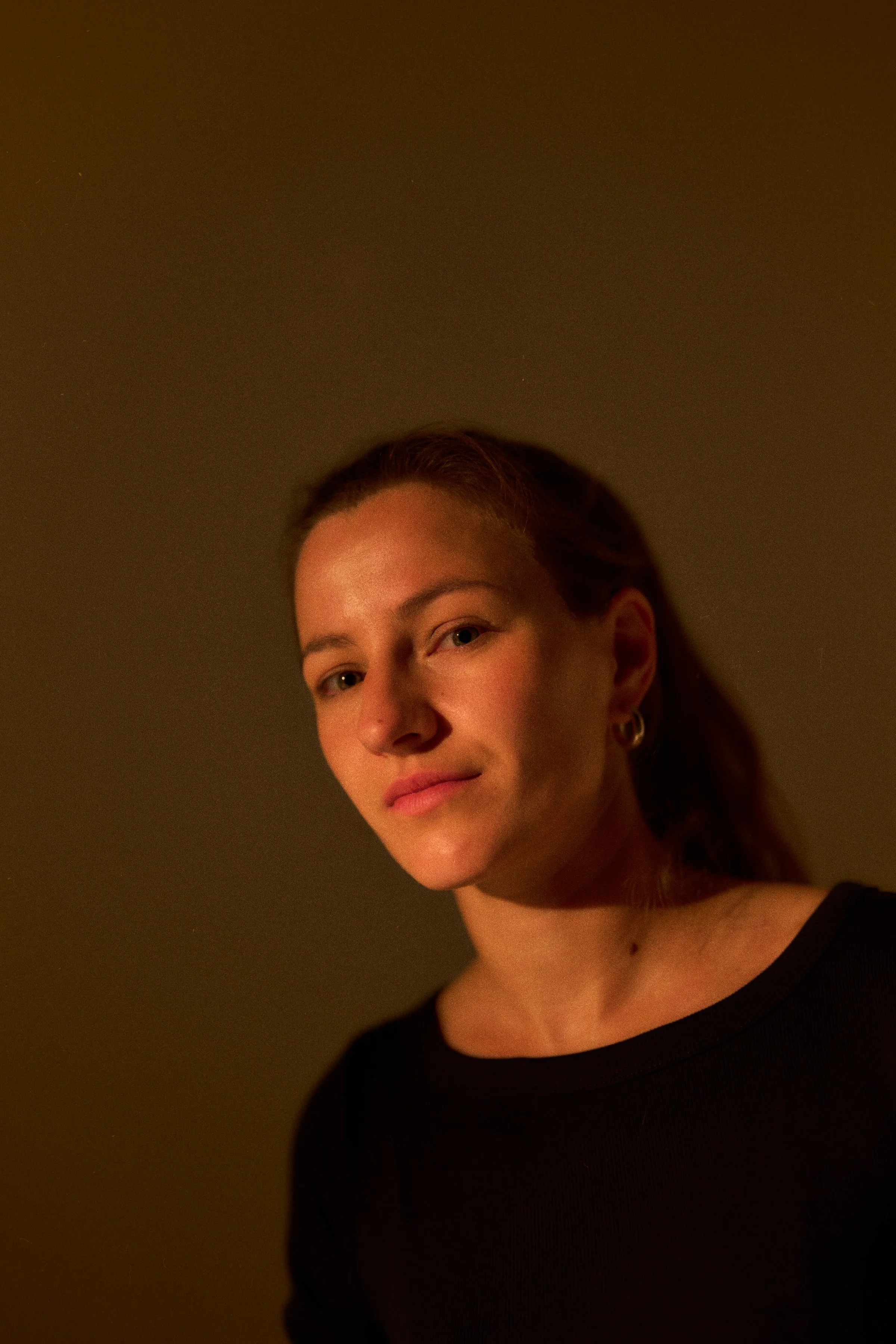 Porträt von Lea, Yogalehrerin bei KRUG12, vor dunklem Hintergrund in warmem Licht.