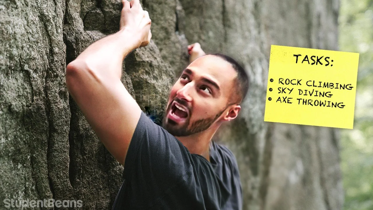 A man with a beard and short hair rock climbing on an outdoor rock wall, with a yellow sticky note that lists tasks: rock climbing, sky diving, axe throwing.