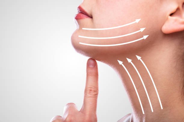Close-up of a woman pressing her finger to her chin, with white arrows illustrating facial slimming or contouring around her jawline.