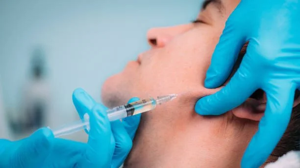 A person receiving an injection in the face from a medical professional wearing blue gloves.