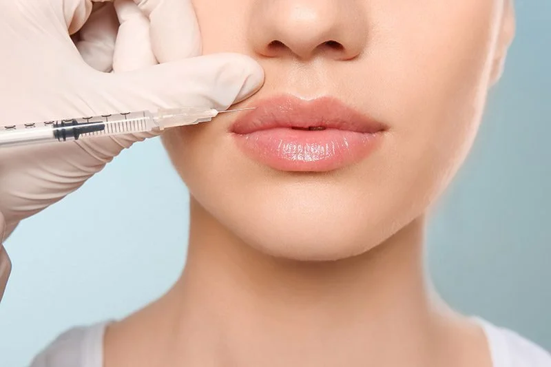 Close-up of a woman receiving cosmetic lip injection with a syringe from a medical professional wearing gloves.