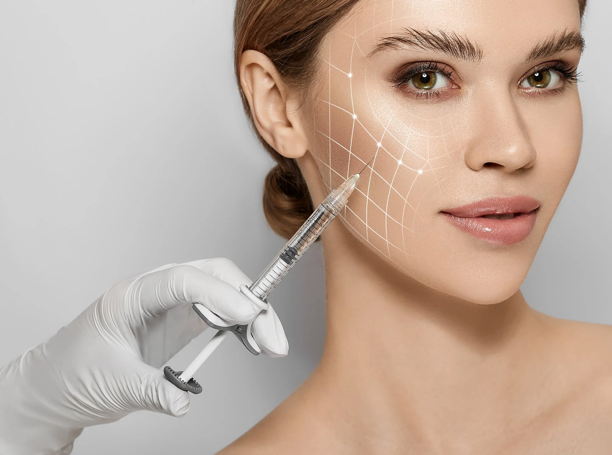 A woman with brown hair and green eyes receives a facial injection from a medical professional wearing white gloves. The woman's skin has a digital overlay showing the injection site with grid lines and sparkles.