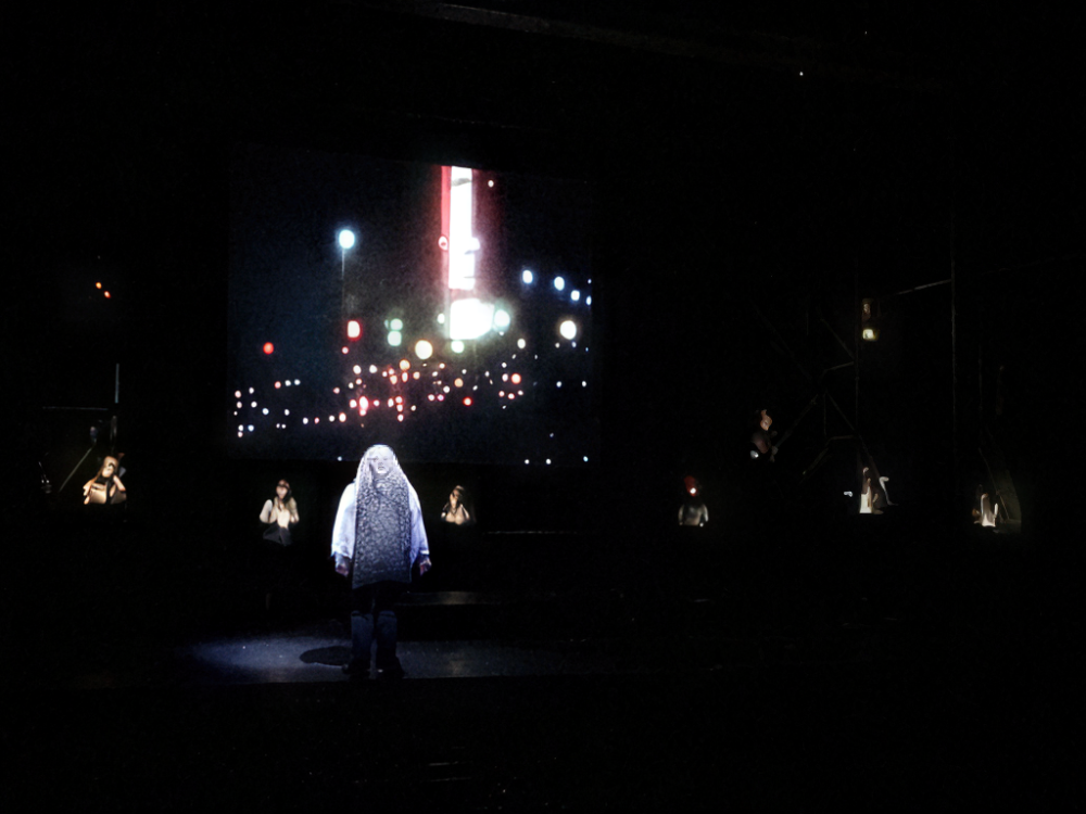 Production photo from a performance of Execution of Justice. A performer addresses the audience sharing their experience of the riots.