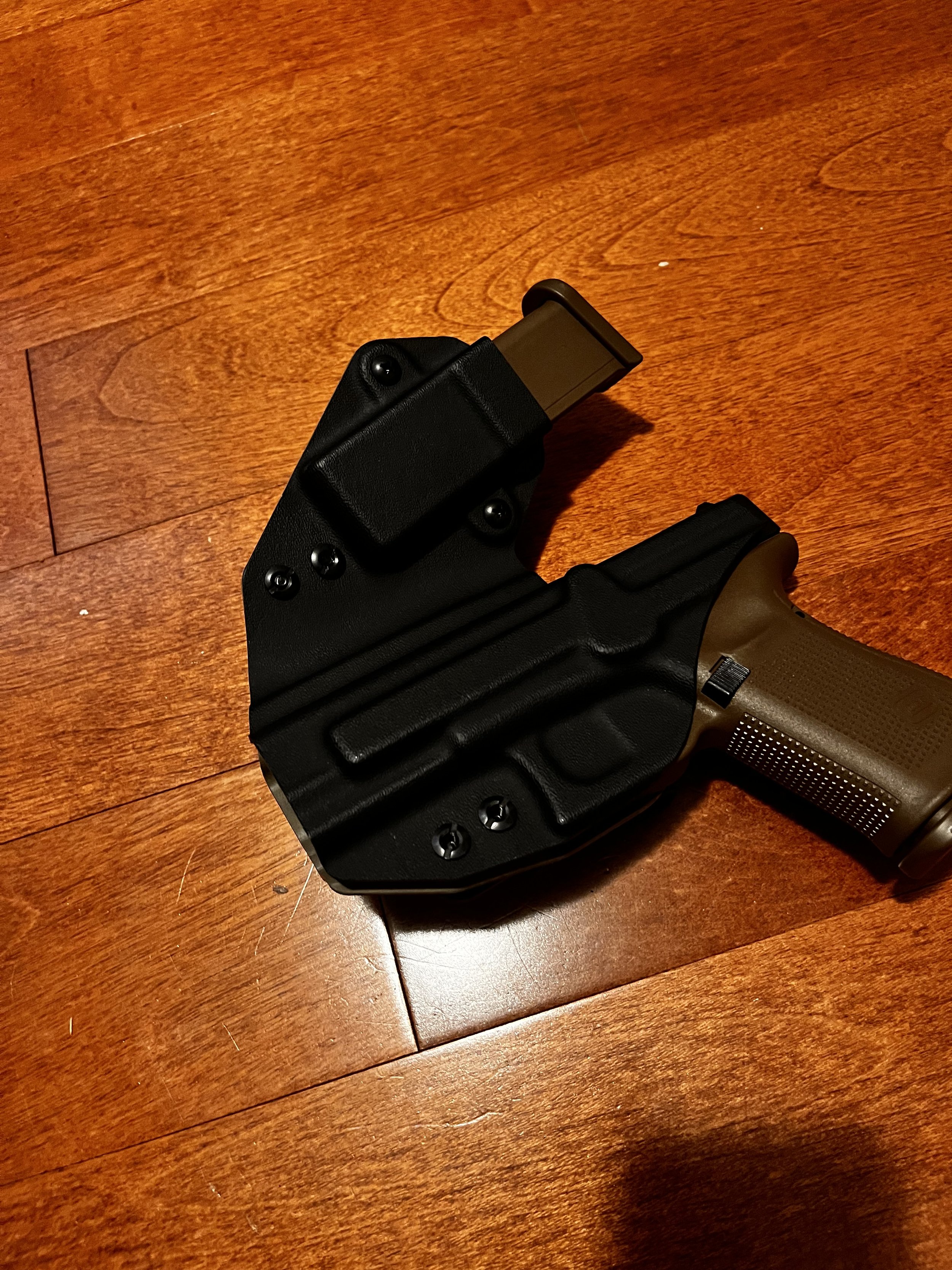 Pistol in black side car holster with an extended magazine, placed on a wooden floor.