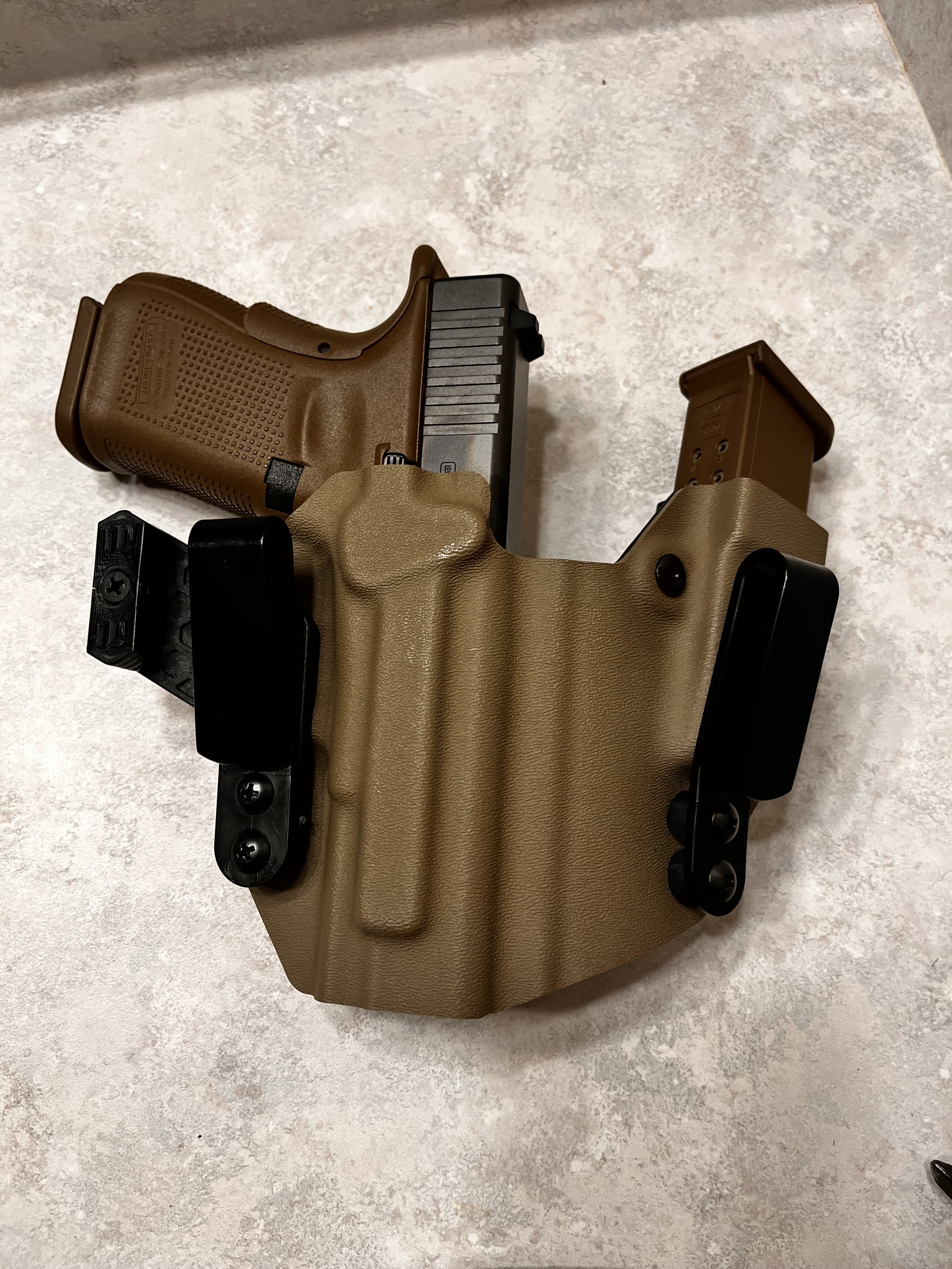 A handgun in a tan holster with a spare magazine, placed on a light-colored surface.