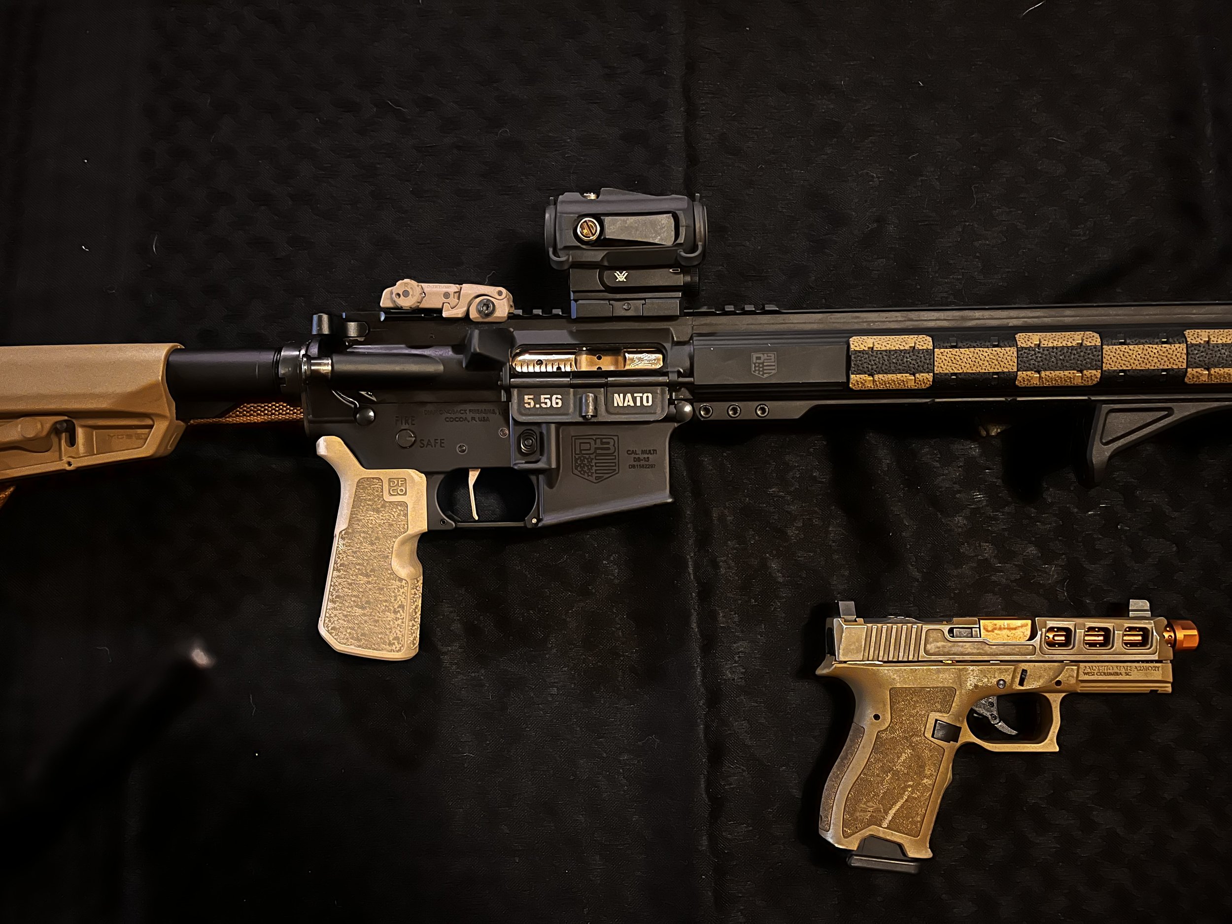 A rifle and a handgun displayed on a dark background. The rifle is equipped with a scope and custom grips. The handgun is placed below the rifle, featuring a compact design and similar customizations. Both firearms have tan and black color schemes.