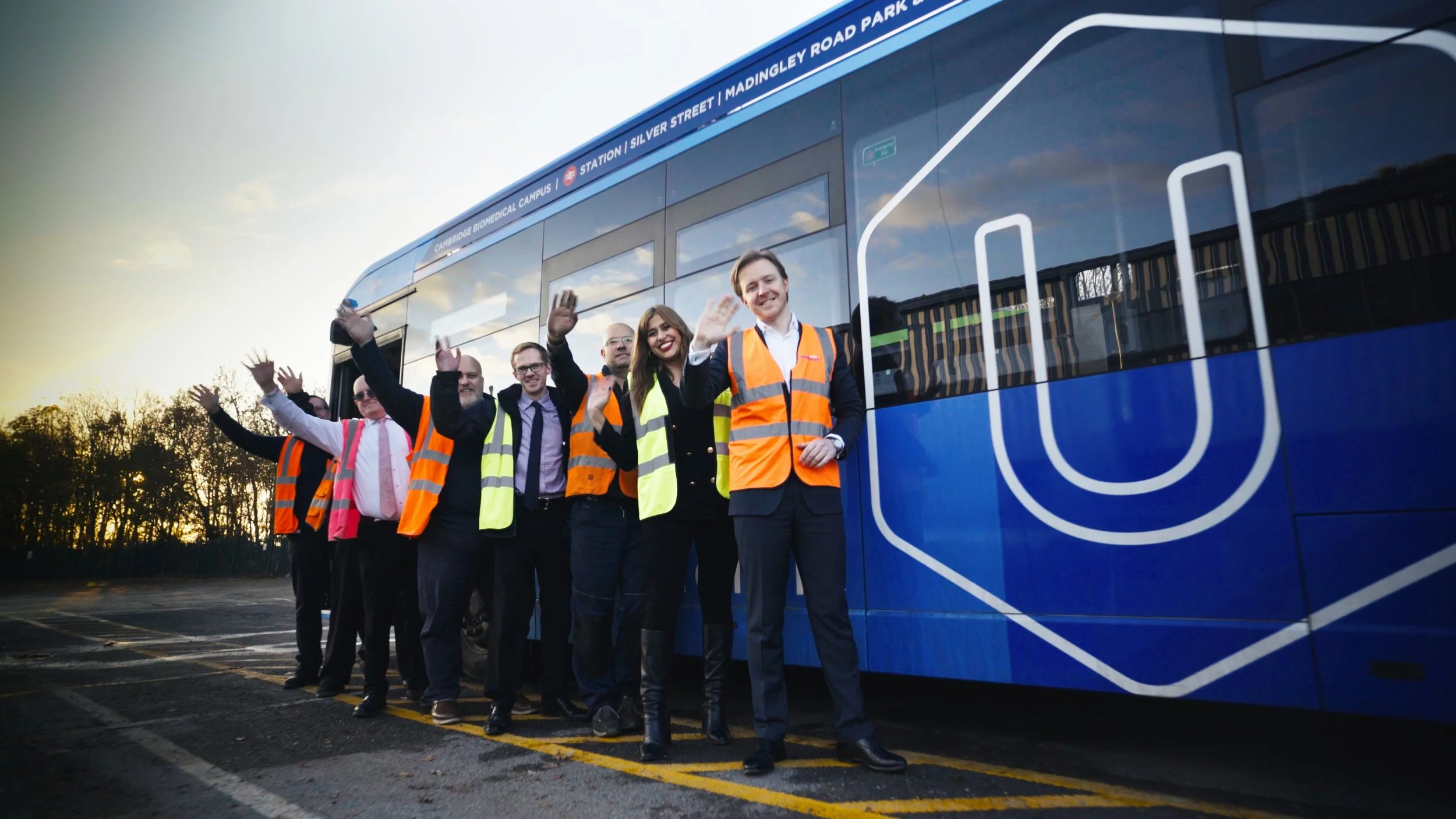 Group of people in safety vests waving next to a blue bus.