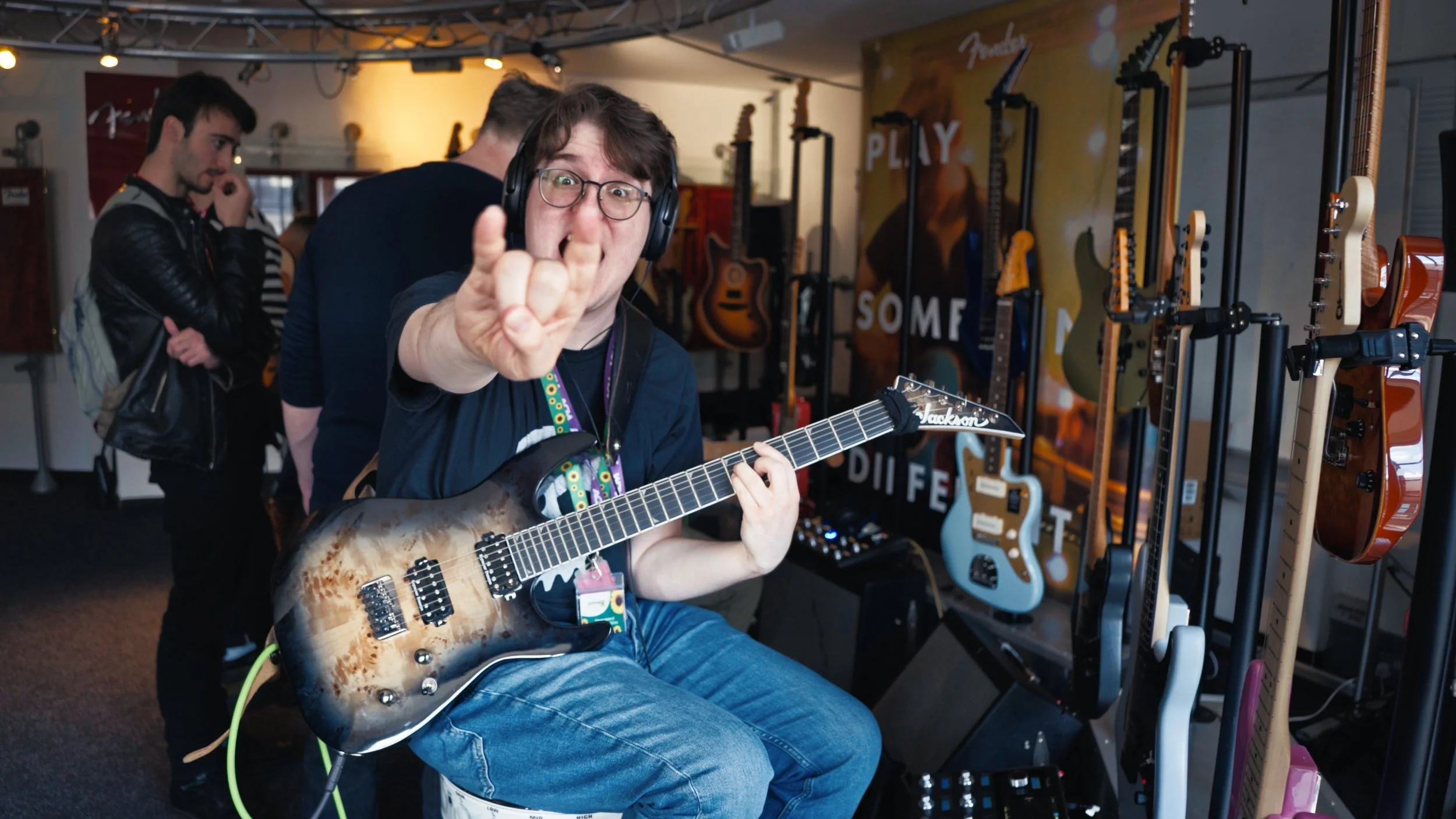 Person playing an electric guitar inside a music store, making a rock hand gesture, with other guitars displayed in the background.