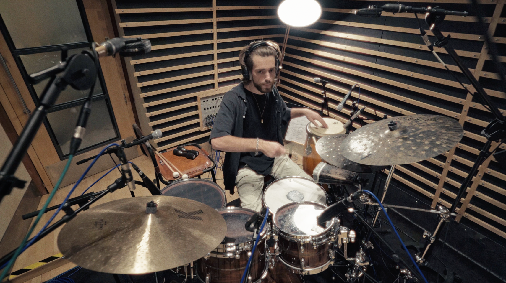 A man playing drums in a recording studio with microphones and soundproofing panels.