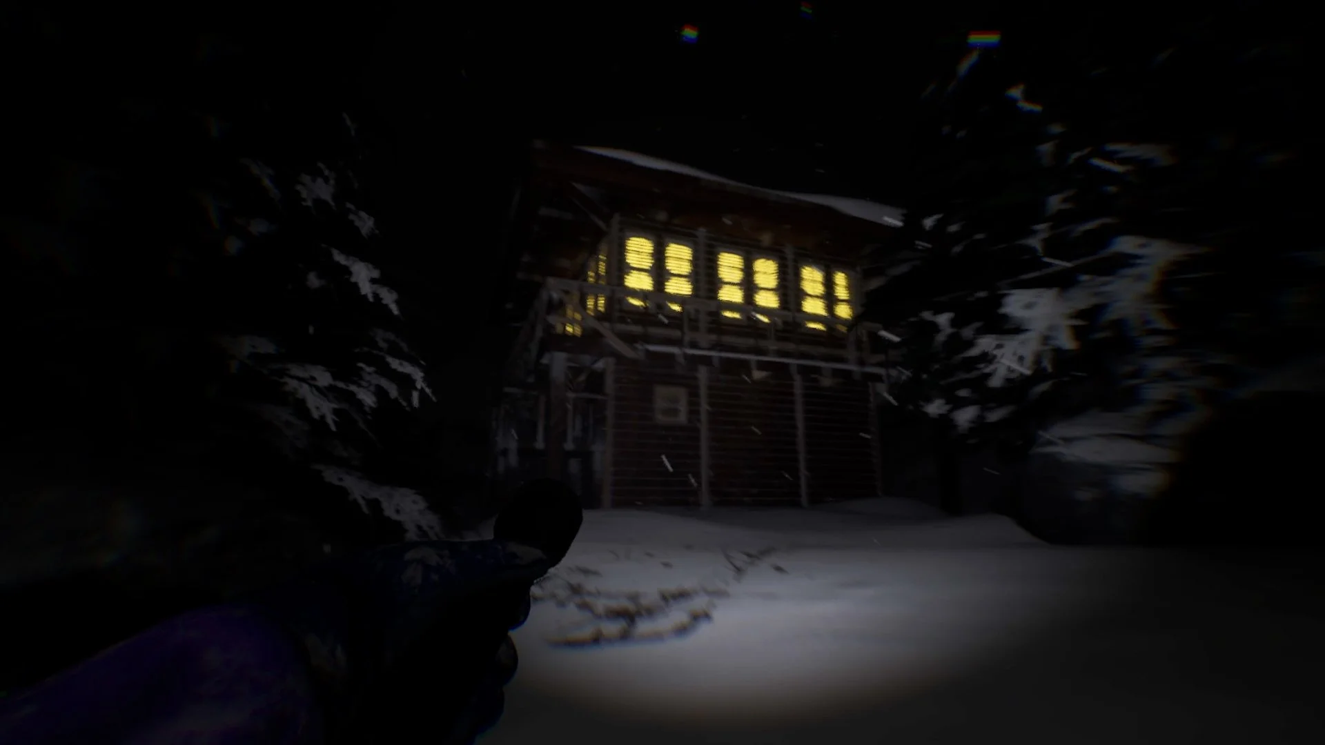 Dark night scene showing a snowy ground and trees, with an illuminated wooden cabin or outbuilding in the background.