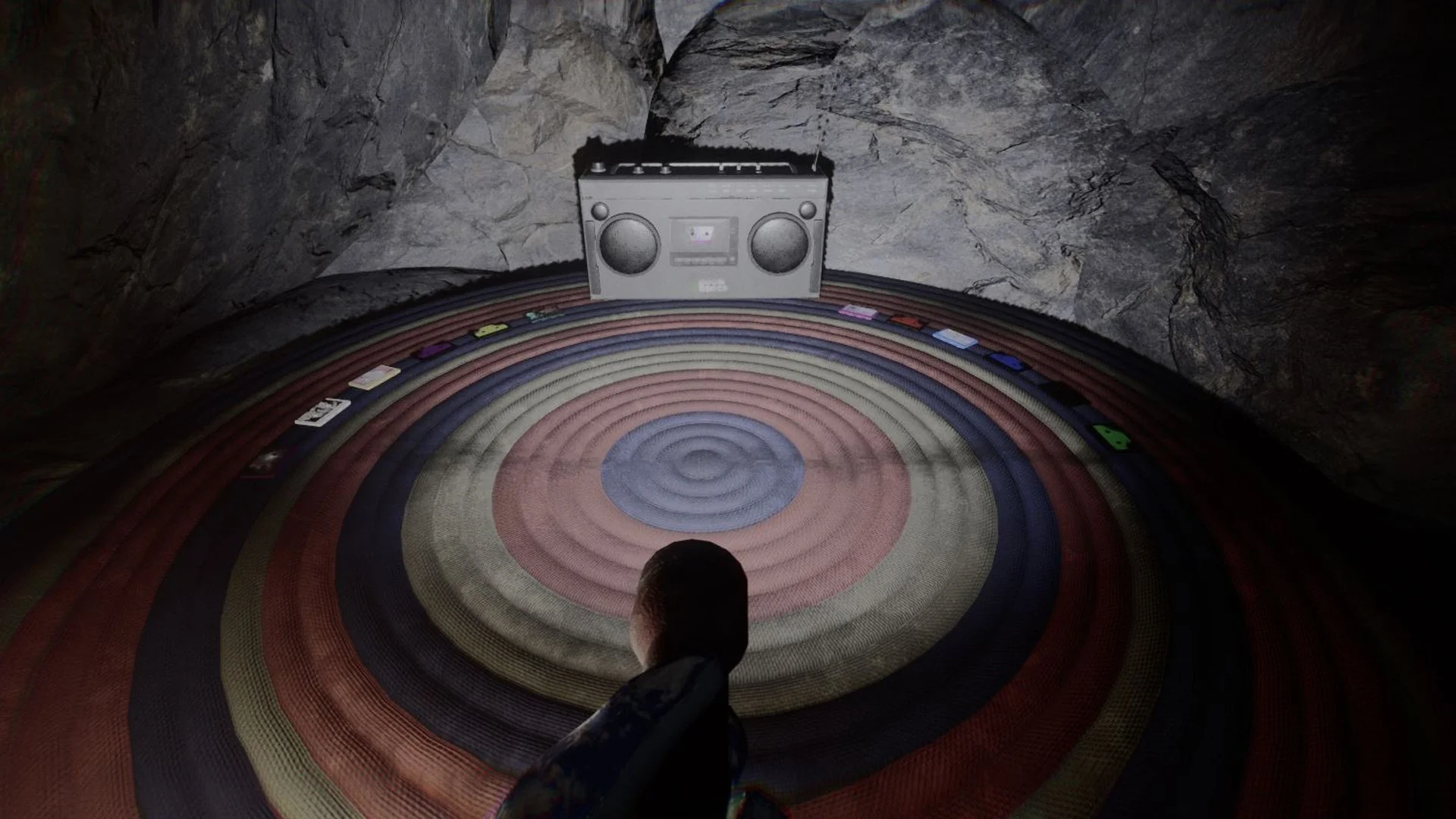 Person facing a circular, multicolored rug with a portable stereo on a rocky wall in a cave.