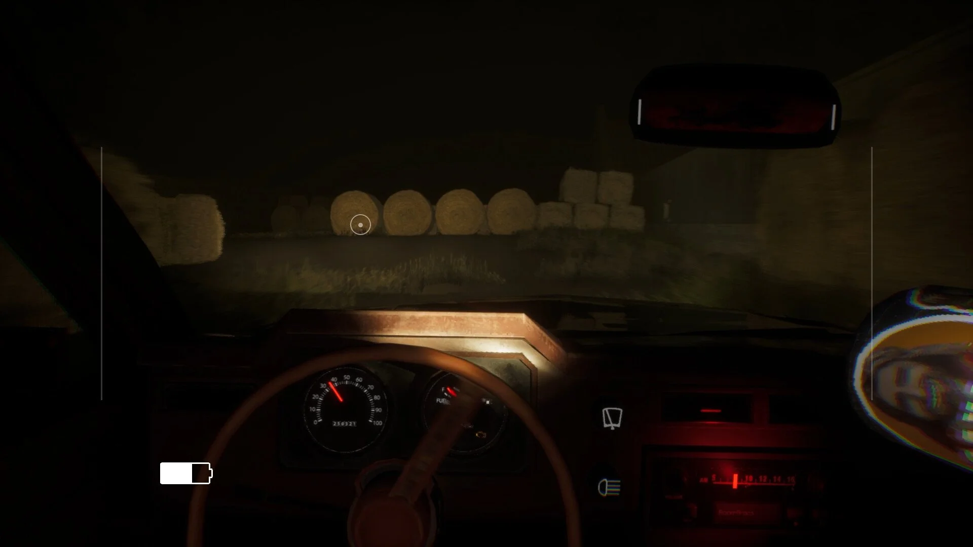 View from inside a vehicle at night showing hay bales on a farm road ahead.