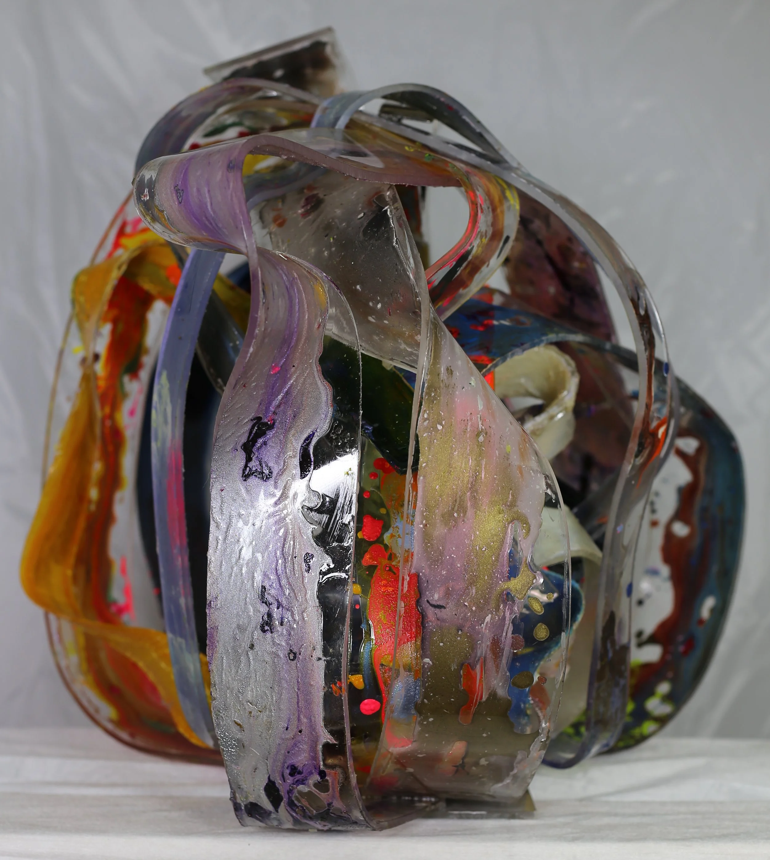 Contemporary abstract sculpture made of layered, transparent acrylic sheets with splashes of paint and metallic details.