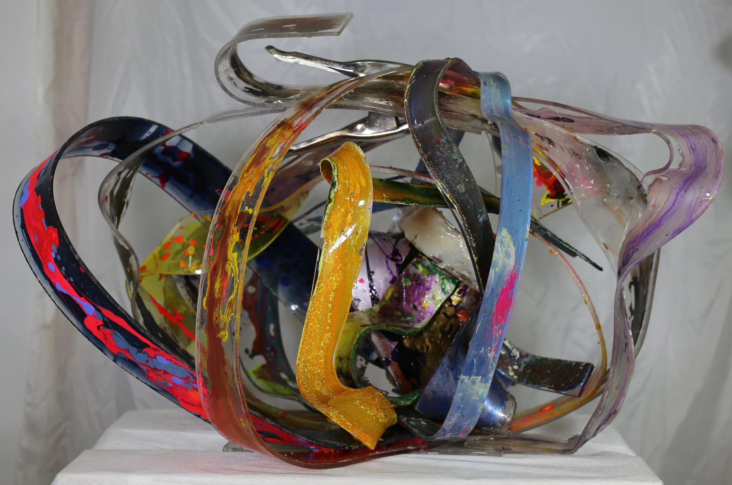 Contemporary abstract sculpture made of layered, transparent acrylic sheets with splashes of paint and metallic details.