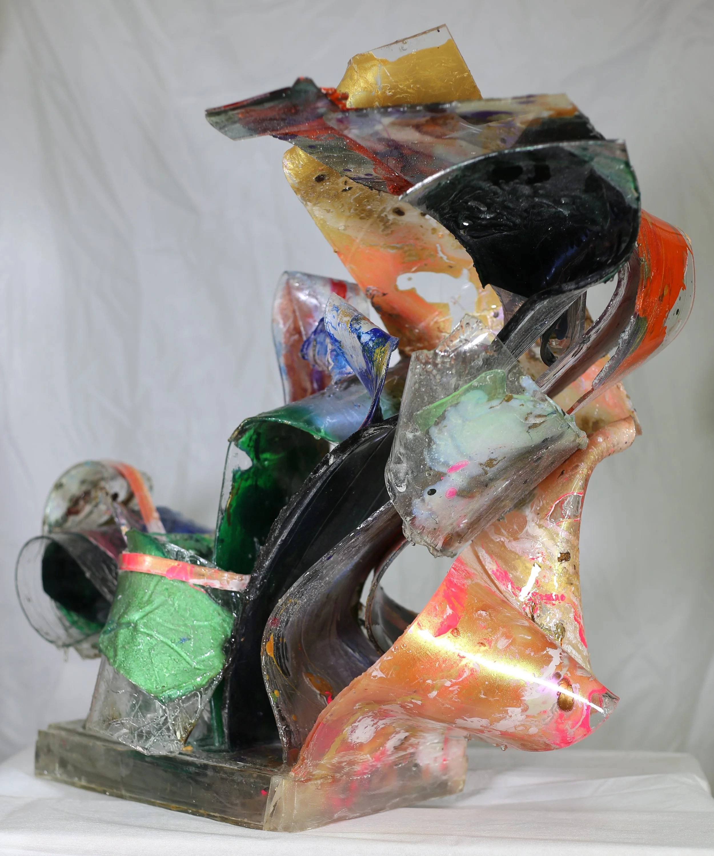 An abstract sculpture made of colorful, irregularly shaped, and textured pieces of plexiglass and resin, assembled into a flowing, organic form.