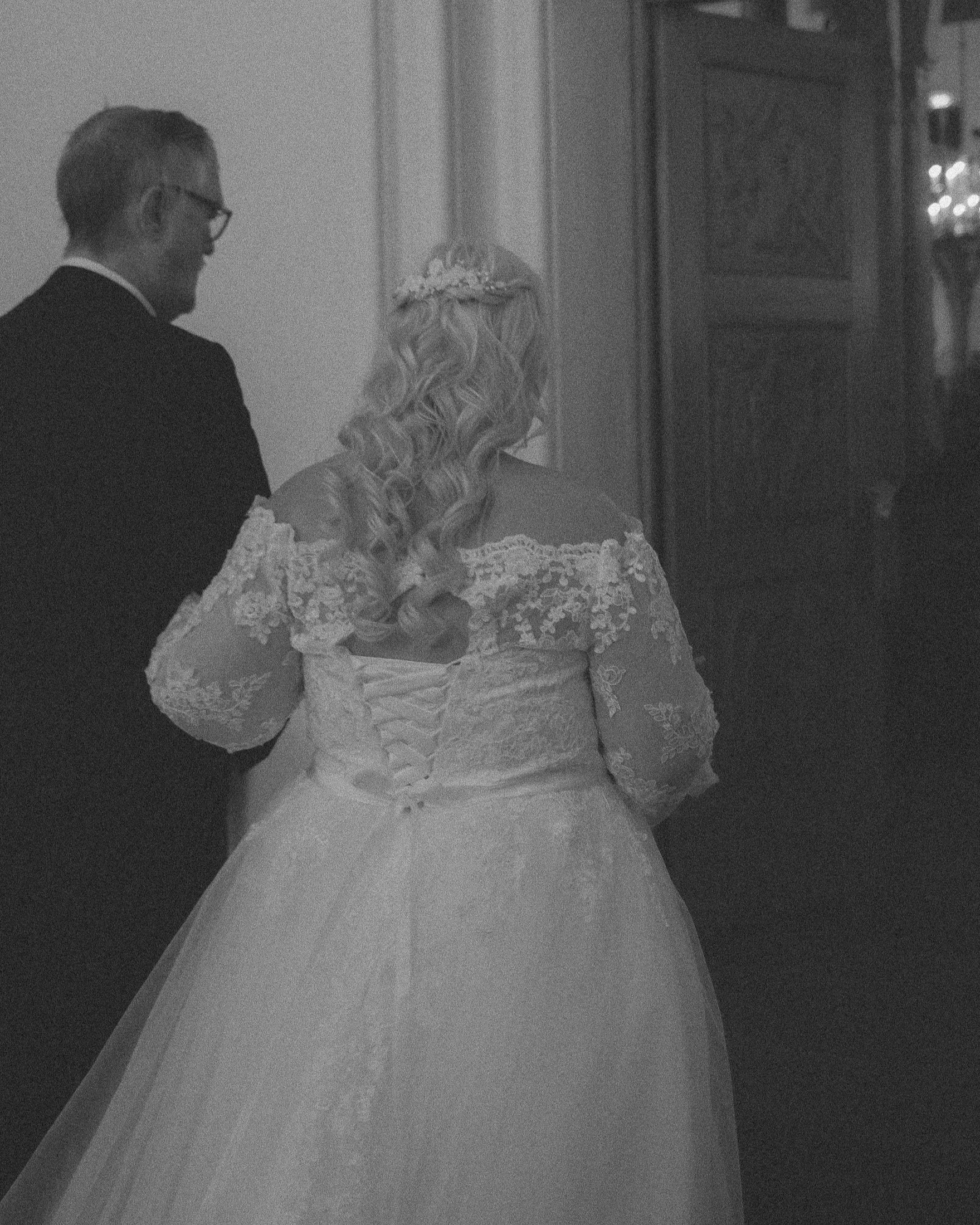 To personer, en mann og en kvinne i brudekjole, står sammen med ryggen til kameraet, på en formell anledning.