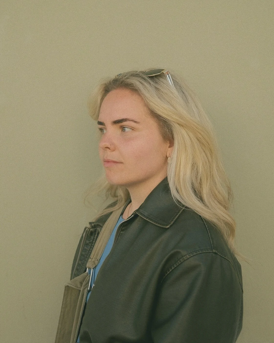 Portrettbilde av en kvinne med blondt hår, iført skinnjakke og solbriller på hodet, med en nøytral bakgrunn.