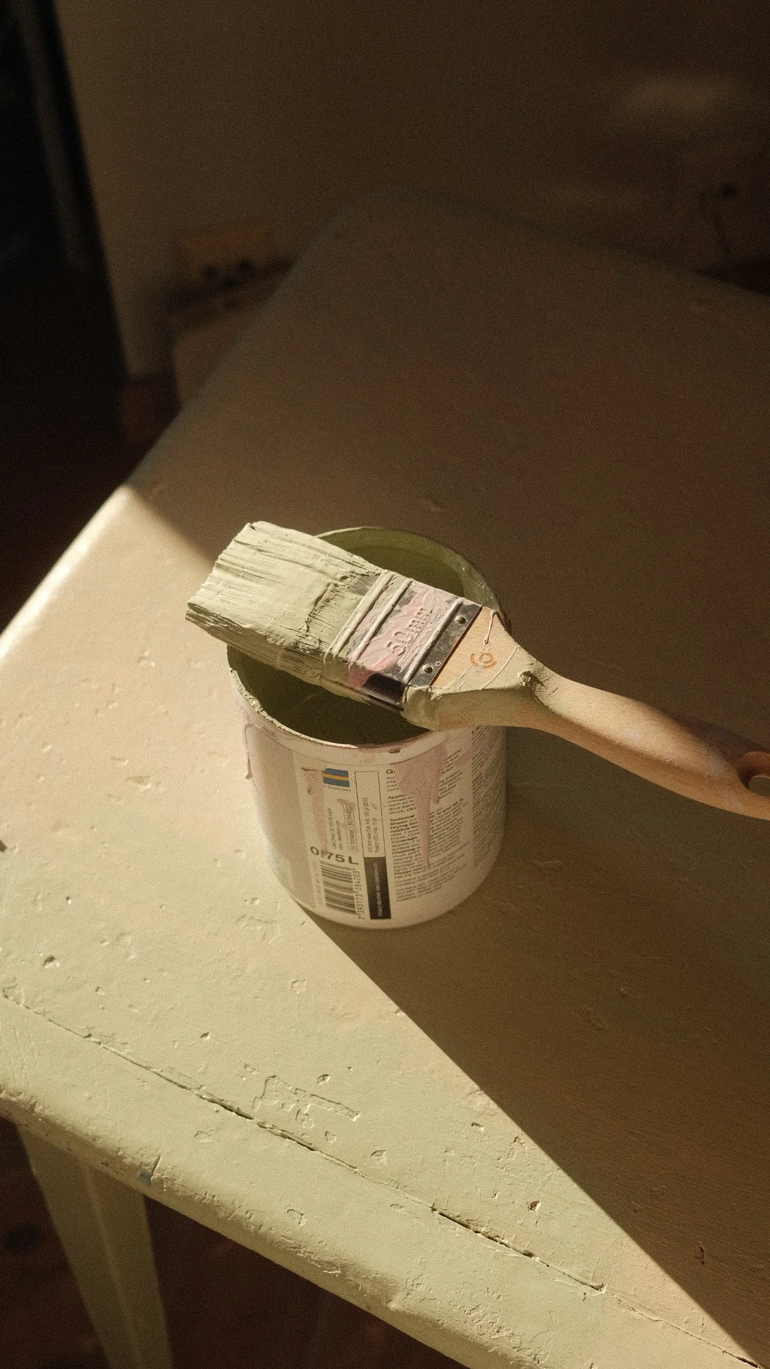 En malingsbøtte med en pensel hvilende på kanten, plassert på en hvit trebord.