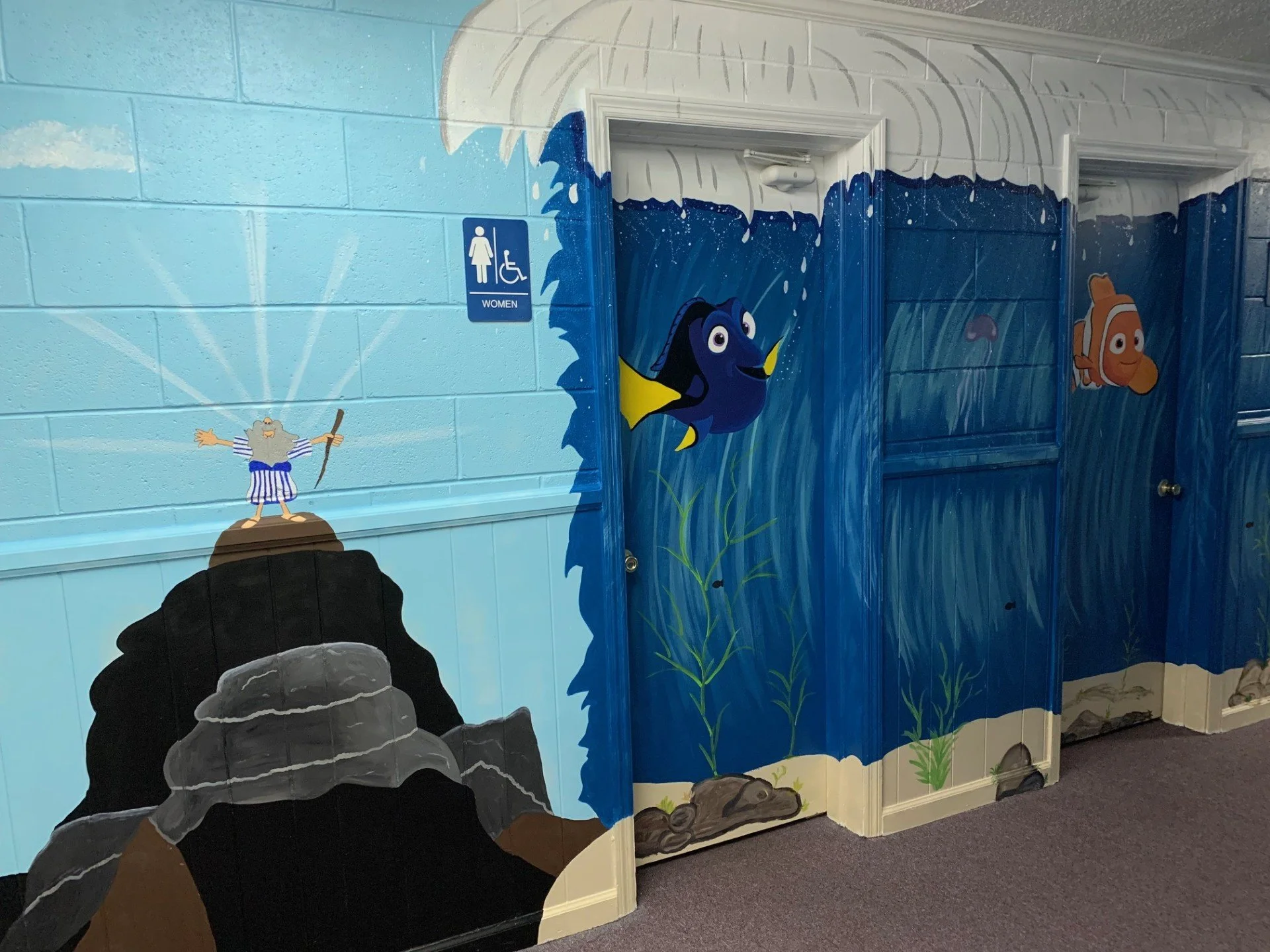 Childcare facility hallway featuring a colorful ocean-themed mural with cartoon characters and a women's restroom sign.