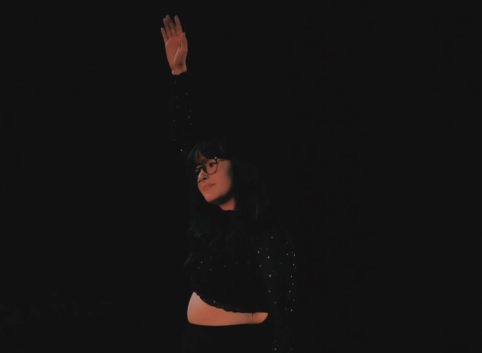 Alexis stands central looking longingly over to the left side of the stage, reaching her hand upwards.