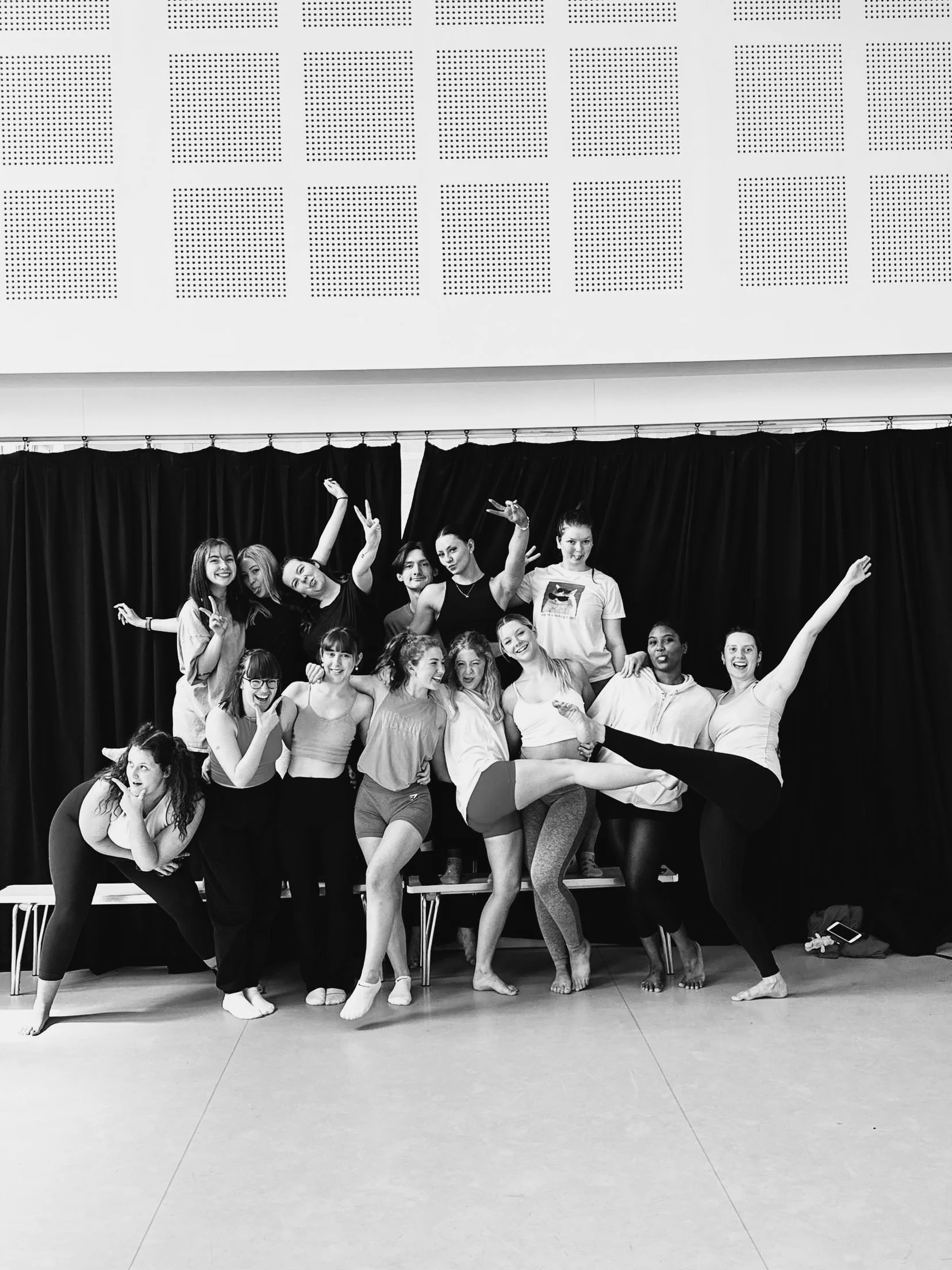 A group of dancers huddle together all posing comedically. They're interlinking arms and celebrating completing their assessed class.