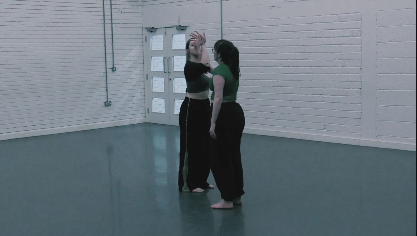 In the dance studio, Alexis and Rai intertwine forearm and hands