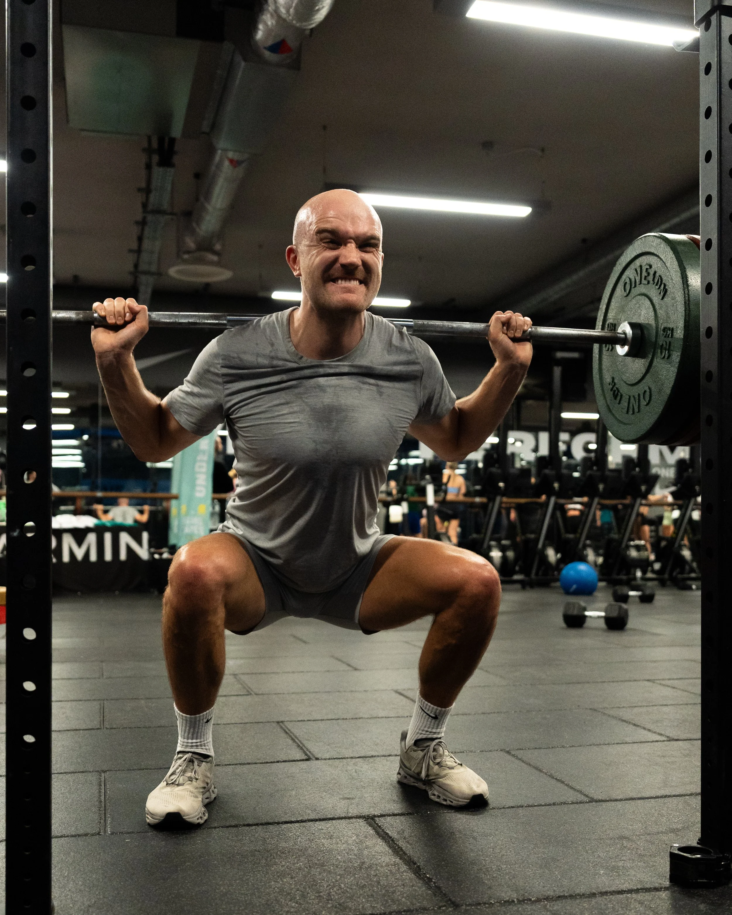 A man lifting a barbell with weights in a gym, squatting with a strained expression.